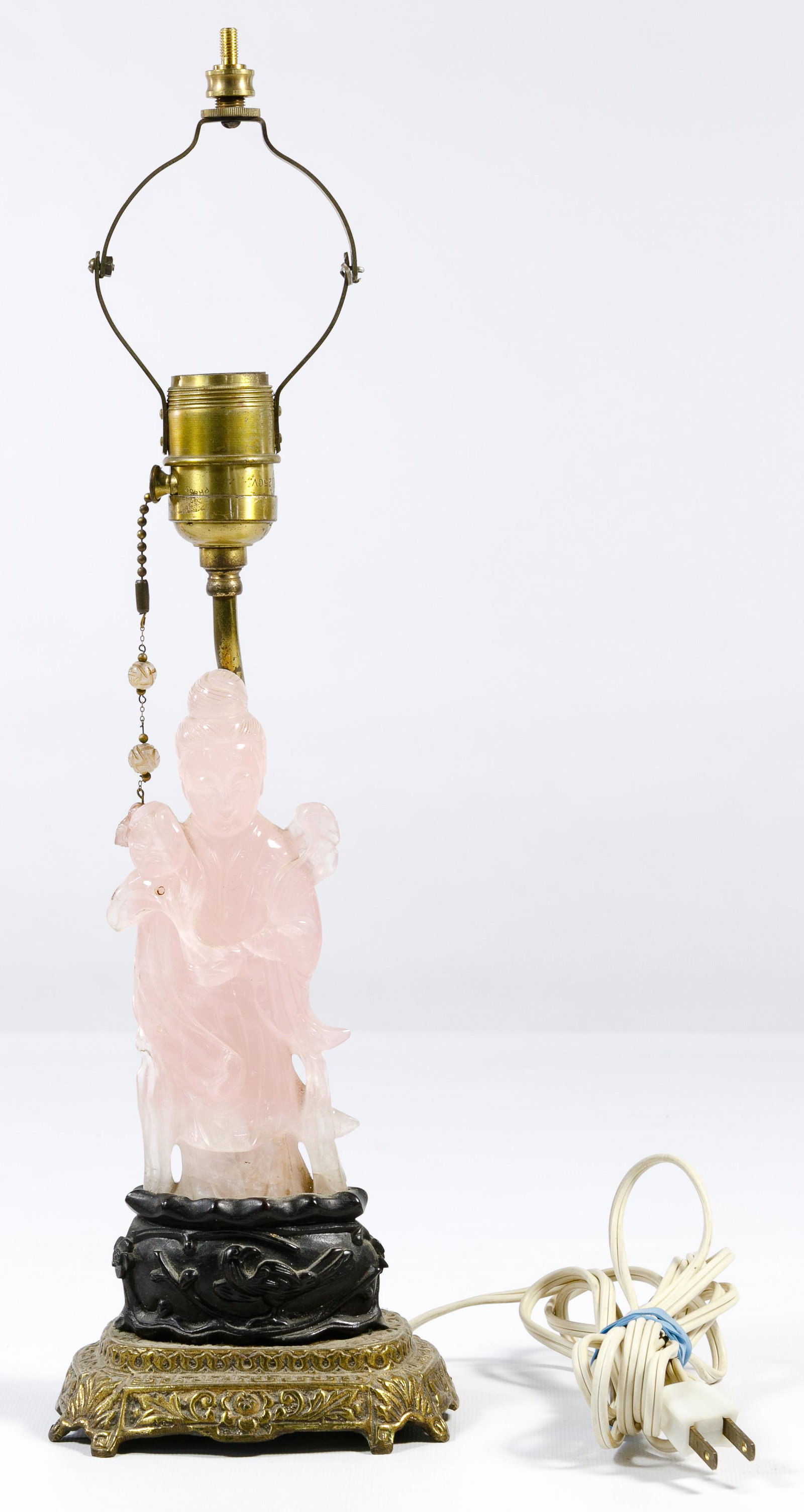 Chinese Guan Yin Rose Quartz Lamp: Chinese Guan Yin Rose Quartz Lamp Carved figure holding a flower atop a carved wood pedestal having a botanical motif, mounted on a brass lamp base having brass hardware and a pull chain strung with c