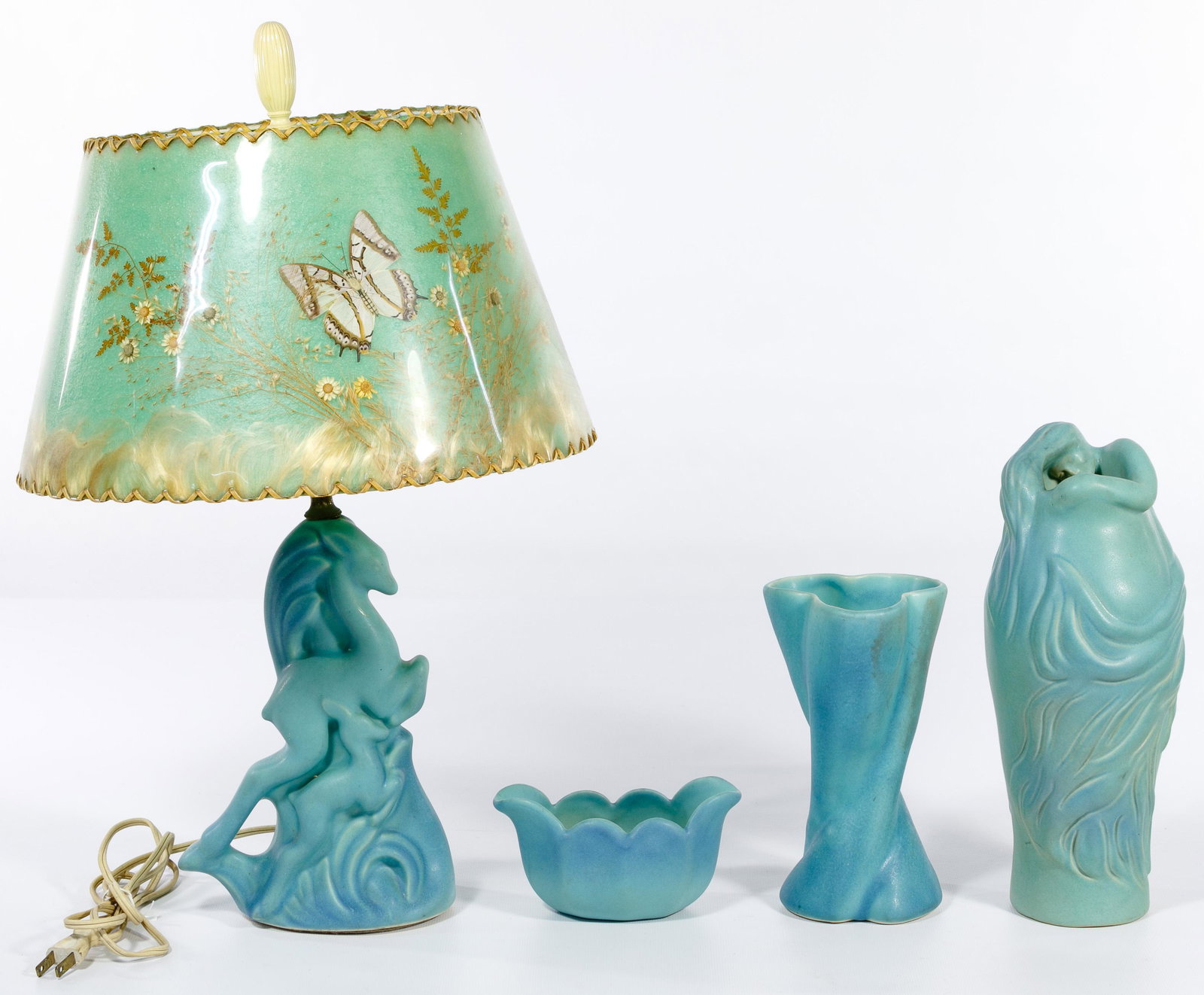 Van Briggle Pottery Assortment: Van Briggle Pottery Assortment (4) bluish green items including a jumping deer lamp having a pressed flower and butterflies lampshade; a vase having a figure of a woman curled around the top of the va