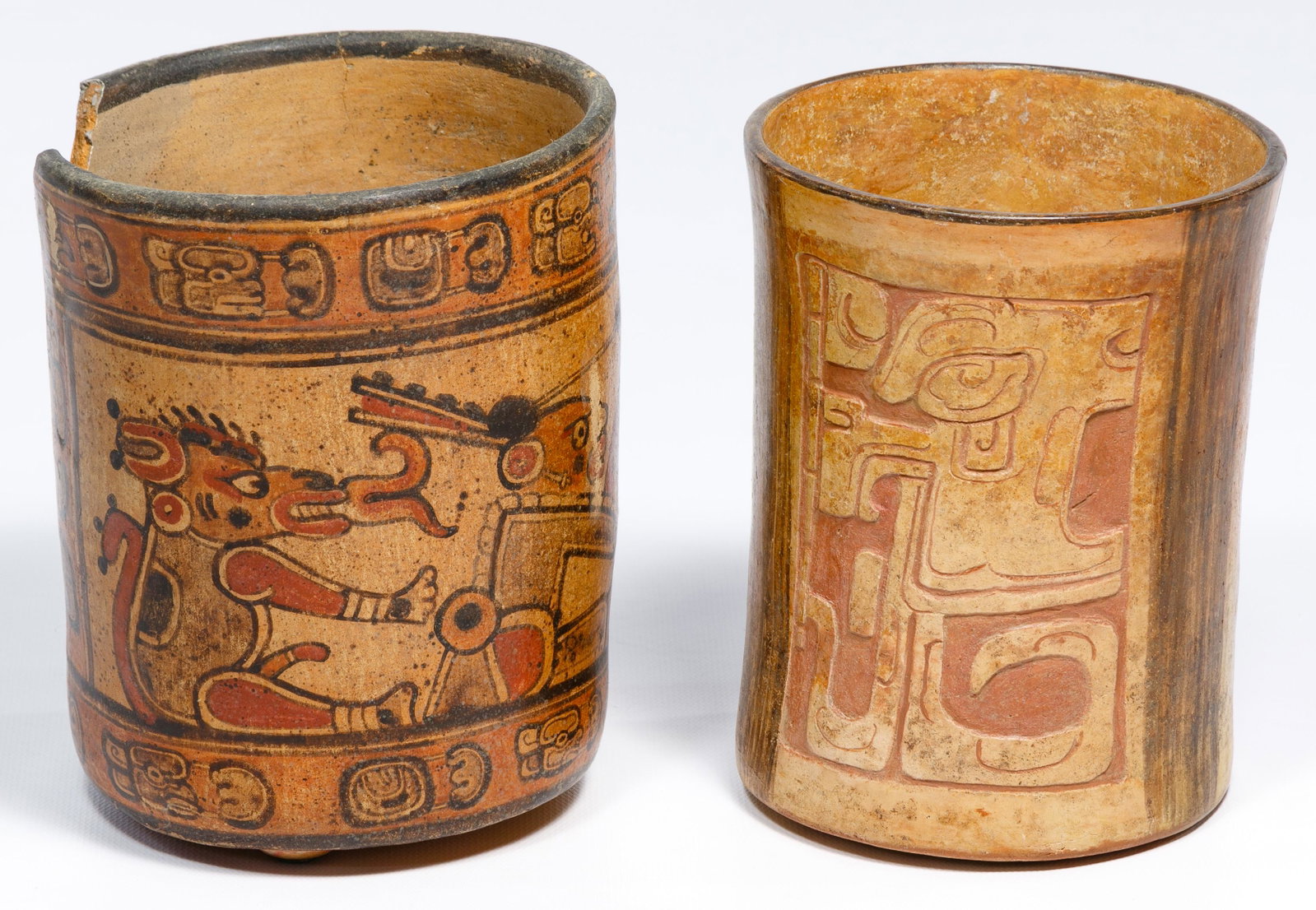 Mayan Cylinder Vases: Mayan Cylinder Vases (2) items including one having carved relief glyphs and the other having polychrome depictions of deities in panels surrounded by bands of glyphs Height: 6 3/8 inches, Diameter: 5