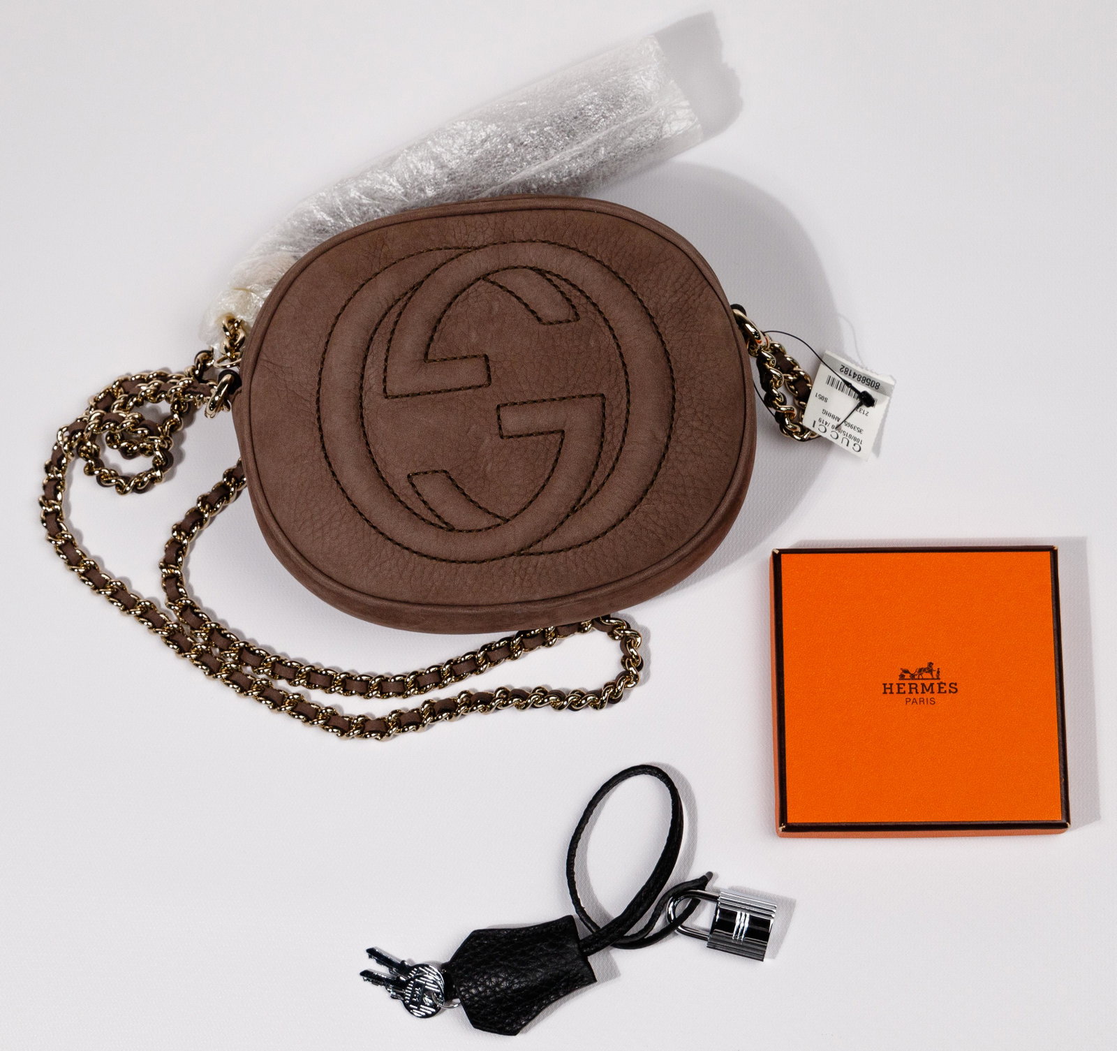 Gucci Handbag with Hermes Birkin Padlock: Gucci Handbag with Hermes Birkin Padlock (2) items including an oval soft taupe signature Gucci Soho having gold crossbody chain, tassel and zipper closure, original box and cloth pouch; and a silver-
