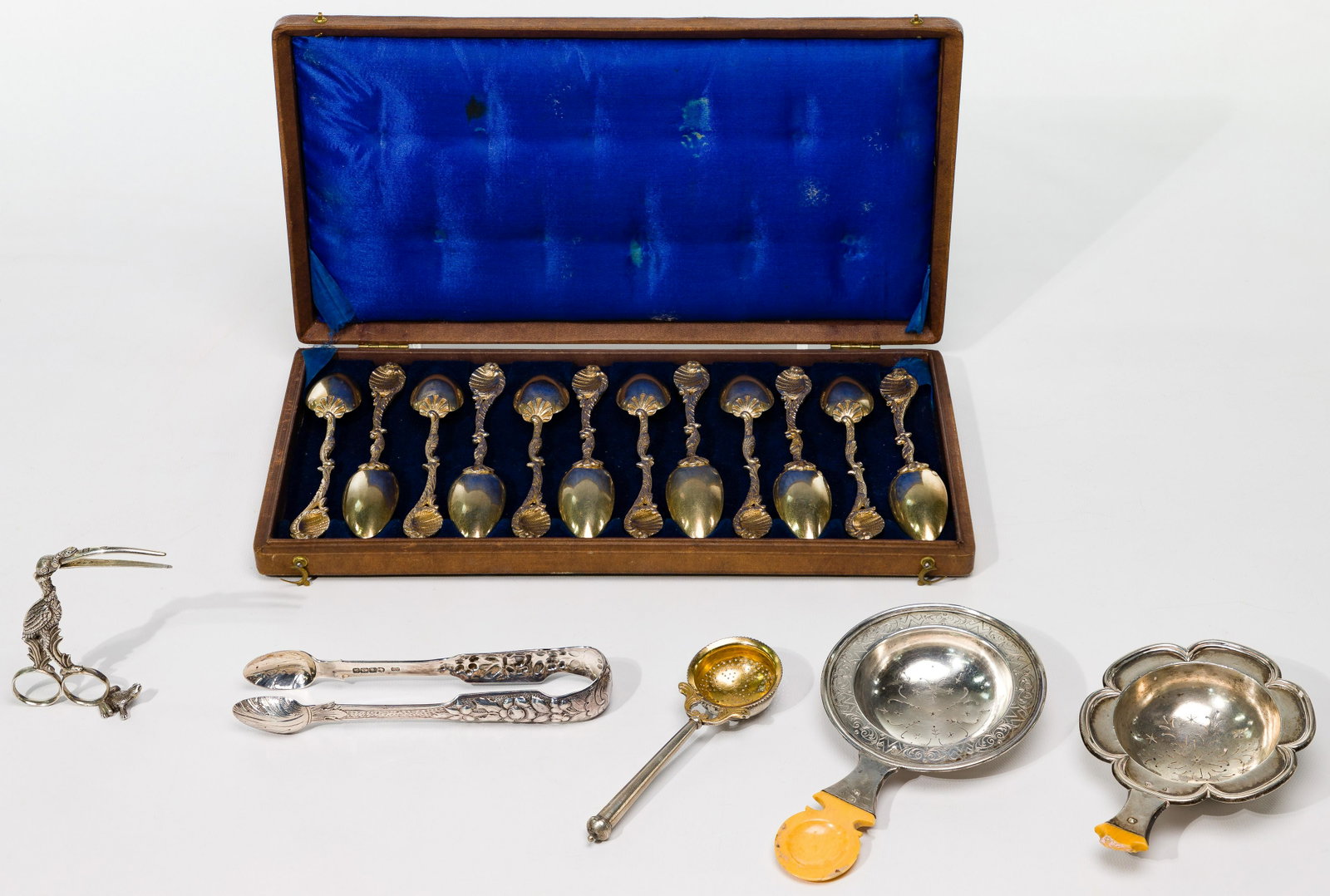 Silver Flatware and Hollowware Assortment: Silver Flatware and Hollowware Assortment (17) items including (12) gold wash ornate spoons marked 'VR' housed in a brown case; (3) tea strainers; tongs with stamped character marks on the inside rim;