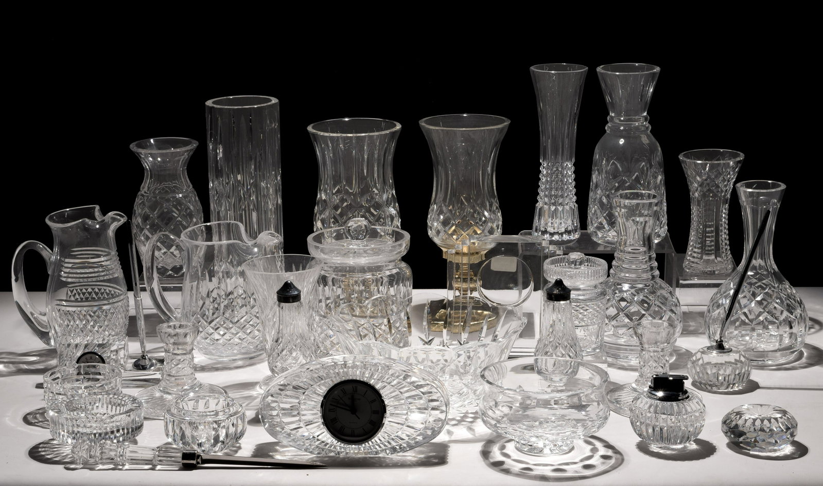 Waterford Crystal Assortment: Waterford Crystal Assortment (28) items including 'Metropolitan' clock; oval desk clock; desk clock and pen holder; 'Prescott' and 'Lismore' brass and crystal hurricane candle lamps; 'Maeve' biscuit j