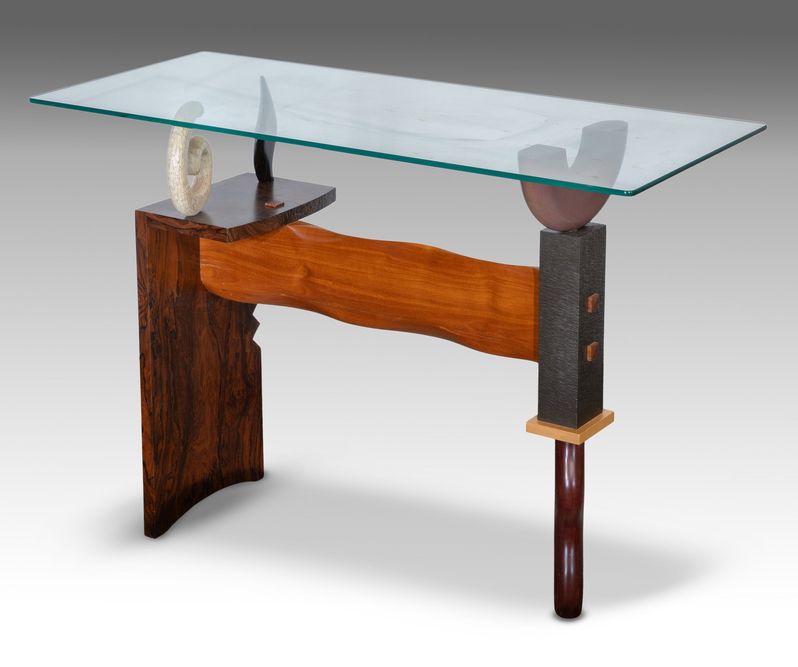 Mark Wallis (American, 20th Century) Hand Carved Accent Table: Mark Wallis (American, 20th Century) Hand Carved Accent Table A sculptural base having a horizontal slab, contrasting joinery, a bleach wood spiral, whimsical cabriole leg and plate glass top,