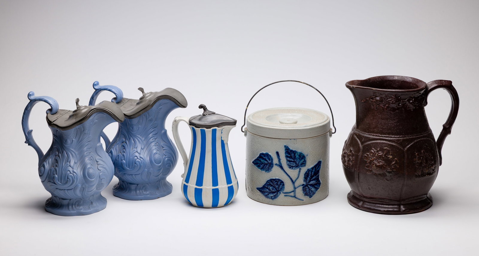 British Pottery Assortment: British Pottery Assortment (5) total items including (2) unmarked Ridgway style relief molded blue pitchers having hinged pewter lids, a Parian ware pewter lidded ribbed pitcher having blue vertical