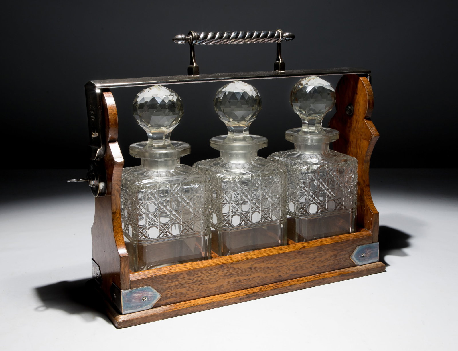 English Oak and Crystal Tantalus: English Oak and Crystal Tantalus c.1880 locking liquor caddy having three square-cut crystal decanters, an oak wood frame, a silver-plated handle, marked Betjemann's on side Property from: an Estate,