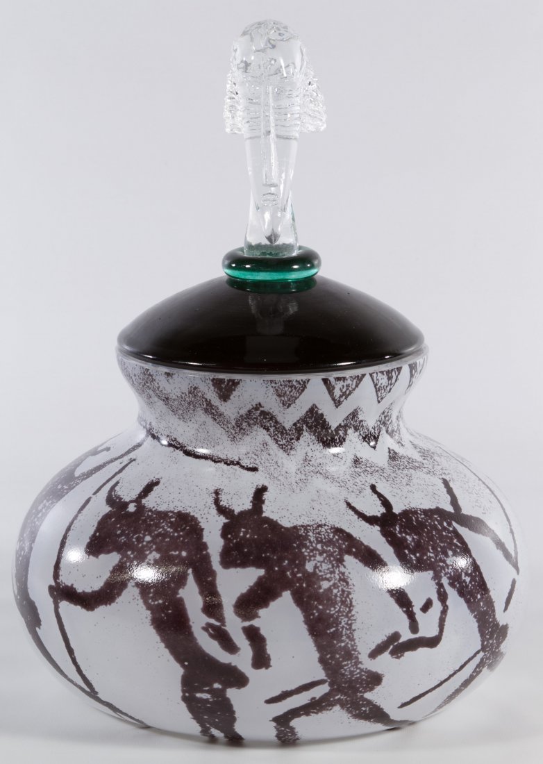 Kosta Boda Bowl by Kjell Engman: Kosta Boda Bowl by Kjell Engman Having a milk glass base with primitive warriors in brown and a clear glass African male bust finial on the green glass lid; and marked on underside Height: 13.00 inche