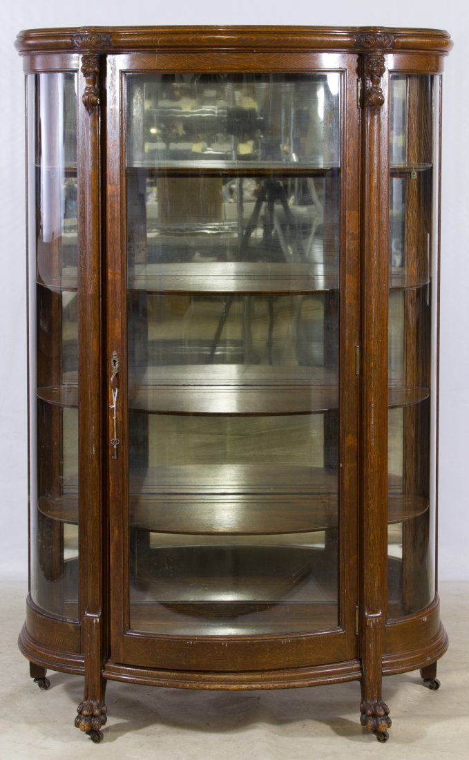 Oak Curved Glass China Cabinet: Oak Curved Glass China Cabinet Having a curved front with lion crowned pilasters, claw feet, castors, glass on three sides and four shelves Height: 64.00 inches, Width: 41.50 inches, Depth: 18.00 inch