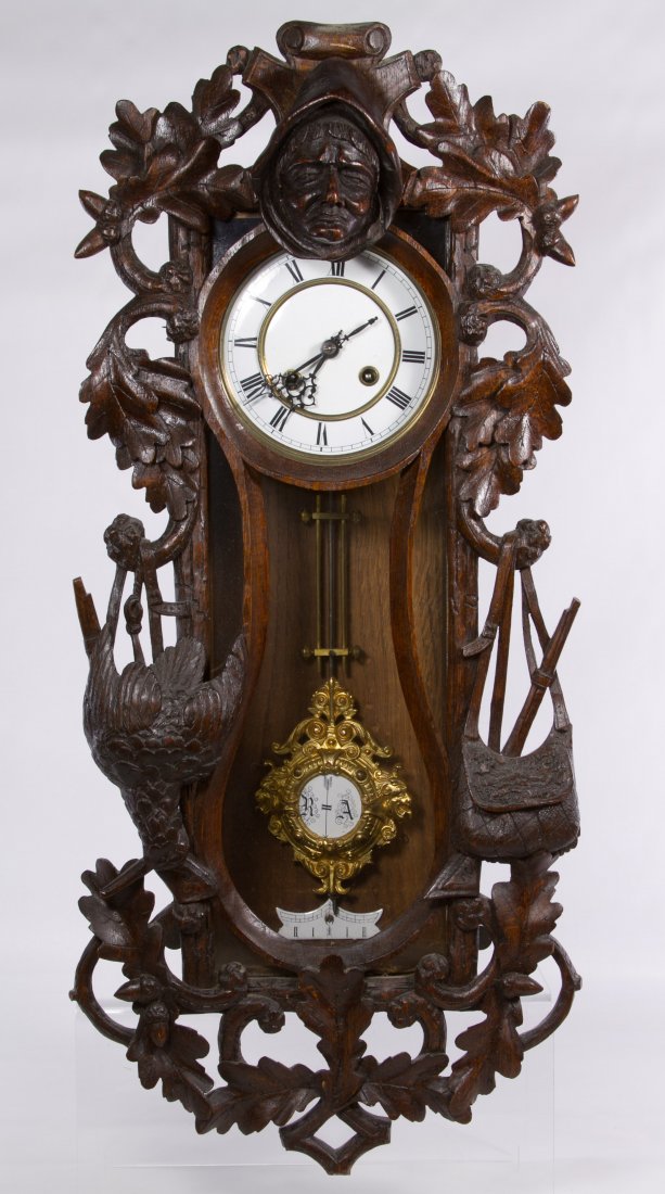 Black Forest Wall Clock: Black Forest Wall Clock Having a hunt theme with a carved bird, rifles, a hunting bag, a death mask and acorns in the wood and glass lid, glass sides, a porcelain dial and an 'R A' marked porcelain pl