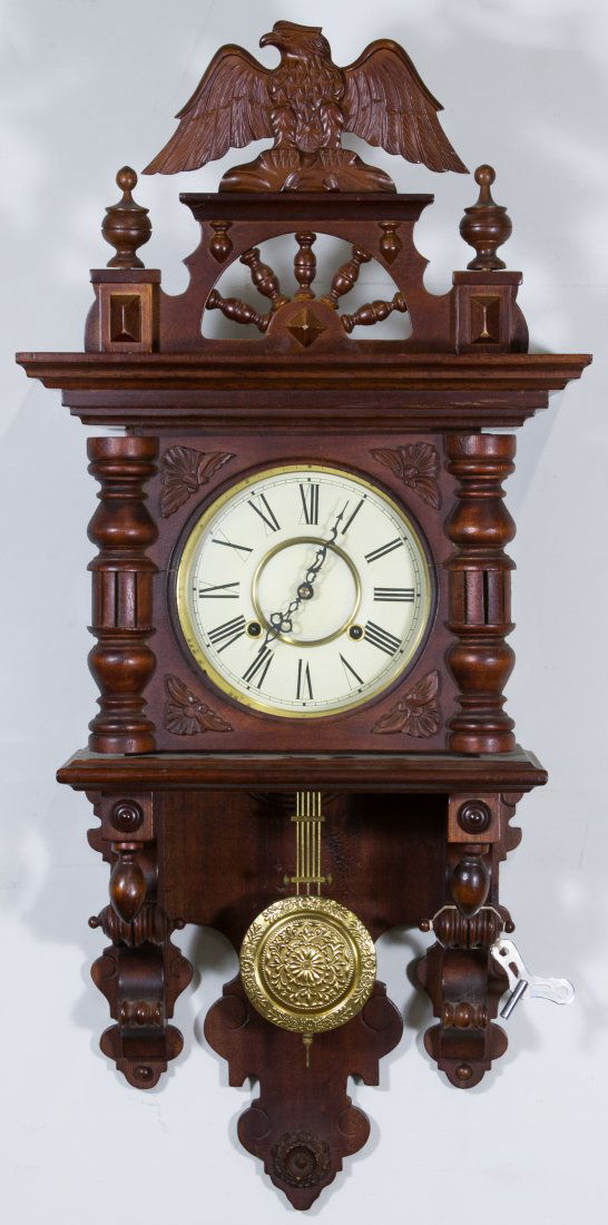Eagle Wall Clock: Eagle Wall Clock Having a cherry stain on the wood case with carved eagle crest and metal dial; including key and pendulum; probably made in Korea Height: 38.00 inches, Width: 17.00 inches Category: D
