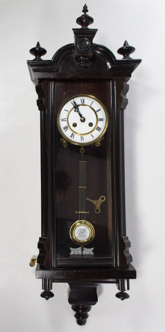 Grain Painted Wall Clock: Grain Painted Wall Clock Having a rosewood painted grain case, an enamel dial and a pendulum with '1886 1986' mark; including key Height: 36.00 inches Category: Decorative Arts > Clocks Shipping Statu
