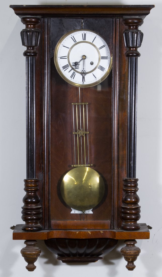 Mahogany Wall Clock: Mahogany Wall Clock Having a porcelain enamel dial with Roman numerals, turned wood pilasters, three glass sides and hanging wood pendants; including pendulum and key Height: 32.00 inches, Width: 17.0