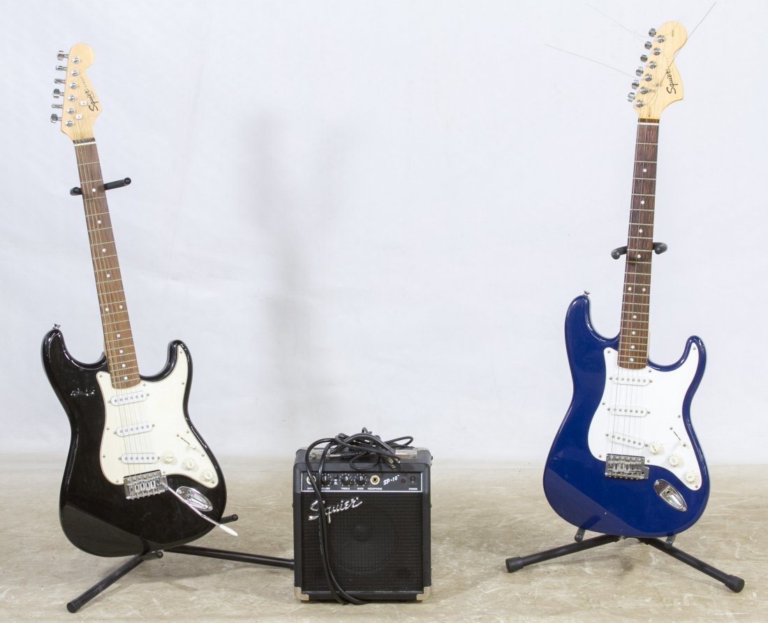 Squier Electric Guitars by Fender: Squier Electric Guitars by Fender Blue 20th anniversary guitar serial #CY20813730 and a black guitar serial #CAE-0030604841; together with two metal guitar stands and a Squier amp serial #AX0381993 Le
