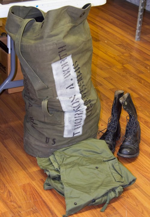 Vietnam Era US Army Duffel Bag and Uniforms: Vietnam Era US Army Duffel Bag and Uniforms Including a large green canvas bag with soldier's name, a pair of boots, a uniform with 'Old Ironside' shoulder patch and additional clothing accessories He