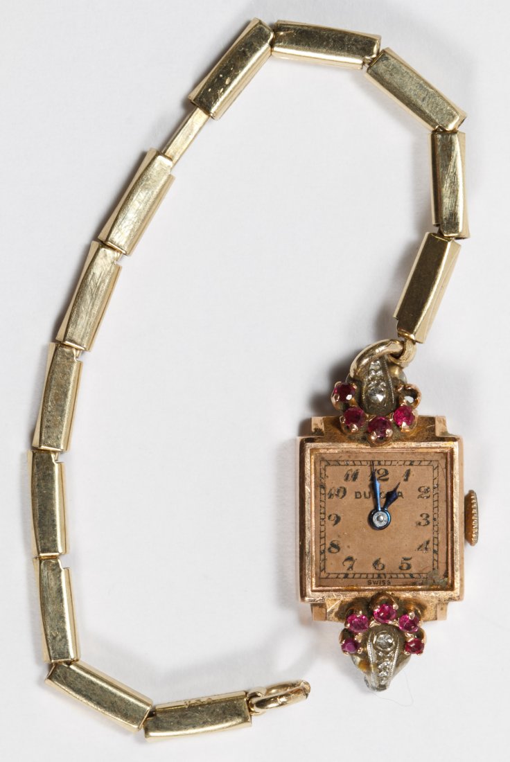 Bulova 14k Gold, Ruby and Diamond Case Ladies Wrist: Bulova 14k Gold, Ruby and Diamond Case Ladies Wrist Watch Having a diamond chip flanked by five rubies on each side; stamped 14k gold mark en verso Length: 6.00 inches Weight: 7.59 dwts. (total weight