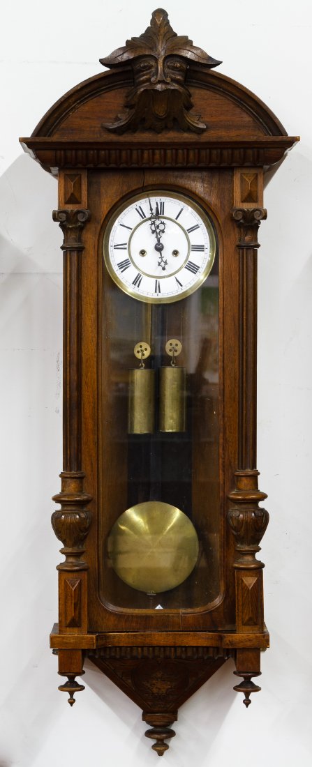 Mahogany Wall Clock: Mahogany Wall Clock Having a porcelain enamel dial, brass bezel, pendulum, key, weights and carved gargoyle mask on crown Height: 47.50 inches, Width: 17.00 inches, Depth: 8.00 inches Category: Decora