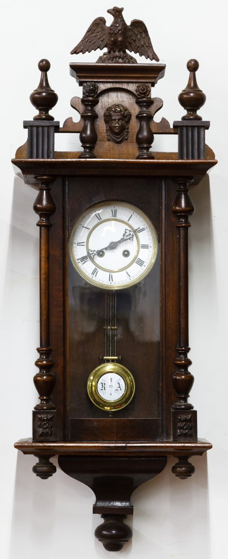 Cherry RA Wall Clock: Cherry RA Wall Clock Having an eagle finial, mask face on crown, porcelain dial, RA marked pendulum and key Height: 35.00 inches, Width: 13.00 inches, Depth: 7.00 inches Category: Decorative Arts > Cl