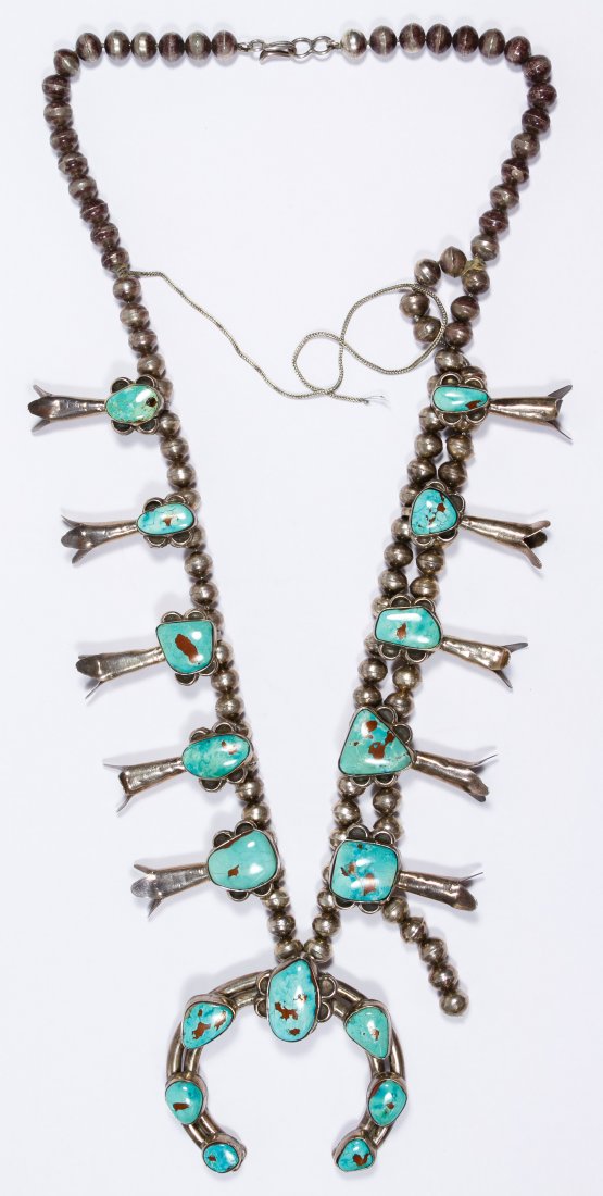 Native American Silver Squash Blossom Necklace: Native American Silver Squash Blossom Necklace Having seventeen free form cabochon turquoise stones with five squash blossoms flanking each side of the central U-shaped leaf medallion Length: 25.00 in