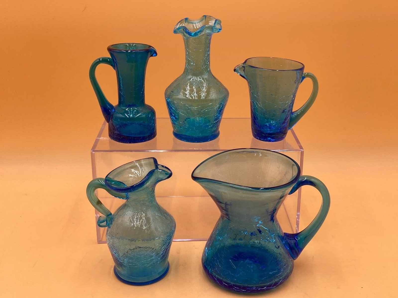 Hand Blown Blue Crackle Glass Creamers: Hand blown blue crackle glass set featuring four creamer style mini pitchers and one swung glass style small vase. Items measure from 4" to 5" tall and are all in good condition.
