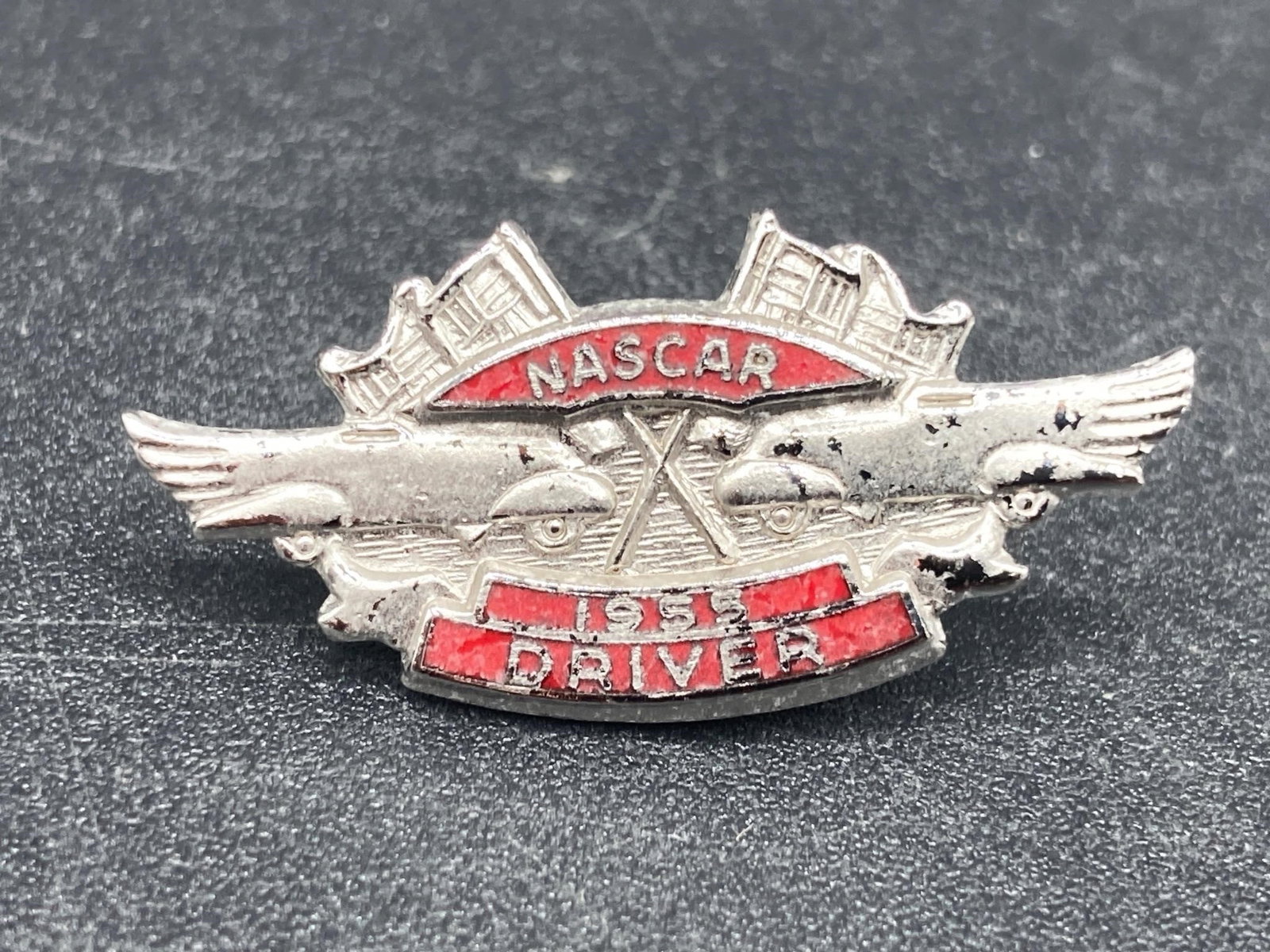 NASCAR 1955 Driver Pin: Rare 1955 nascar driver pin. Silver and red color with vintage flags and cars designs. Some small areas tarnish as noted in photos, otherwise pin is in good condition.