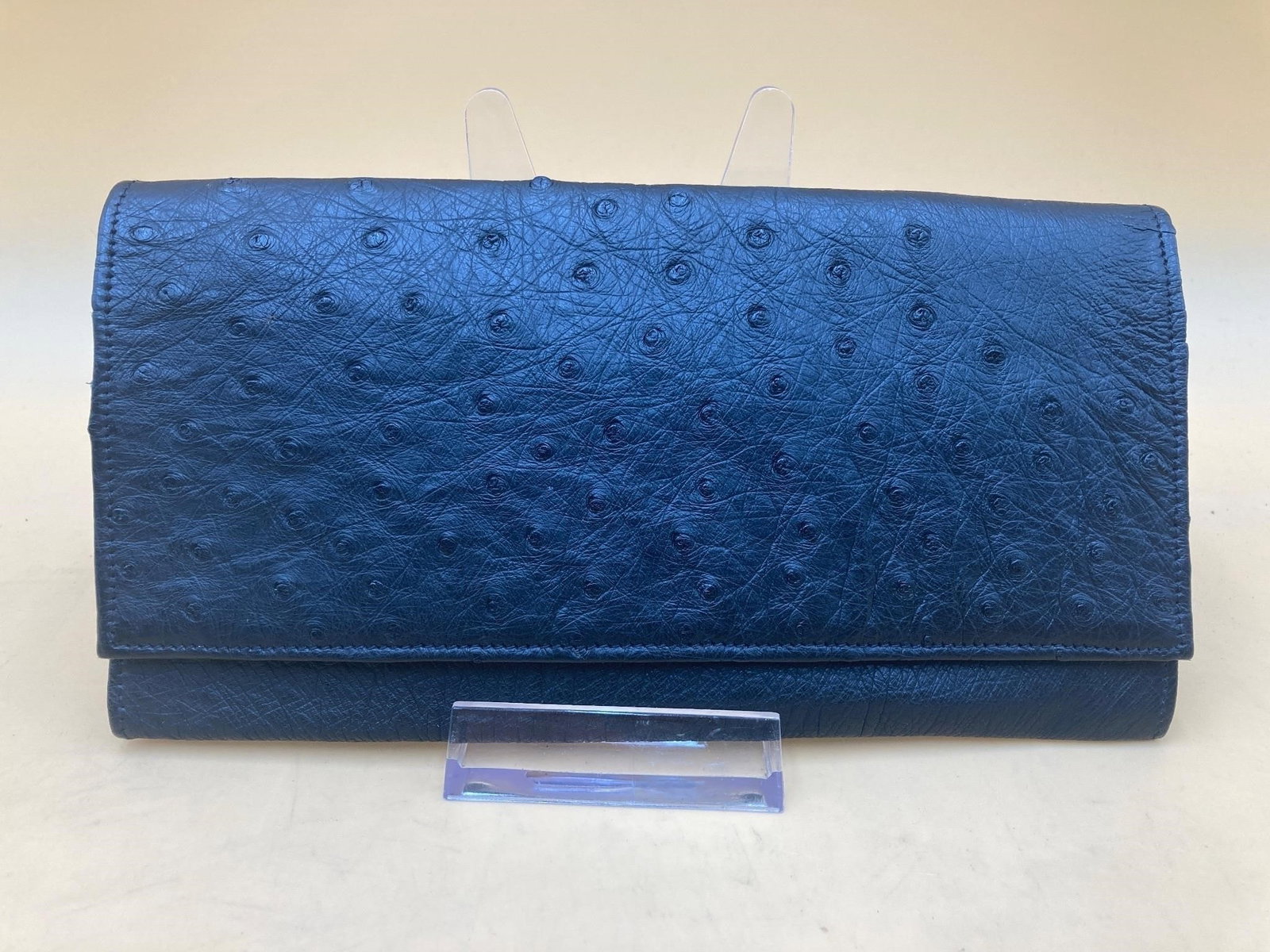 Genuine Ostrich Leather Checkbook: Genuine ostrich leather checkbook wallet. Wallet features three pockets large enough for checks and bill currency, six card slots and one exterior zippered pocket. Wallet is black color and measures 7