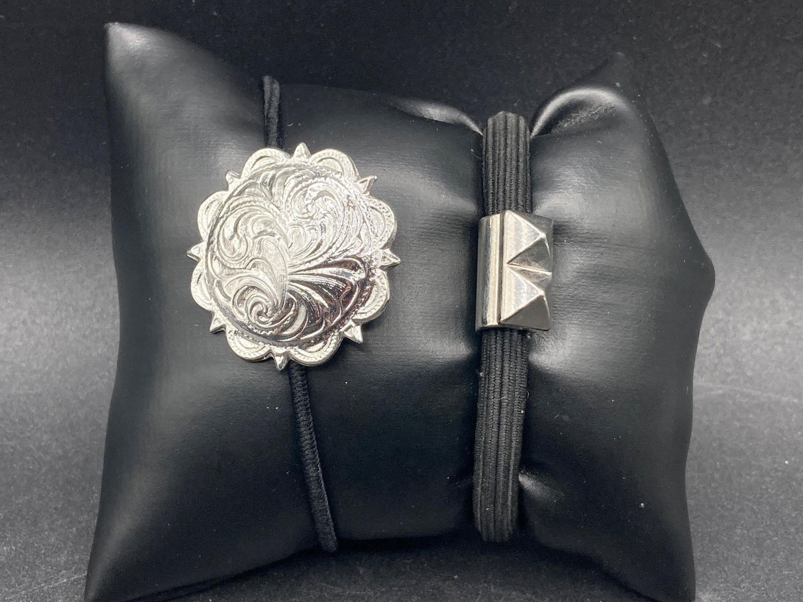 Silver Tone Hair Ties: Pair of silver tone hair ties. One features ornate patterned 1 1/2" medallion shaped charm, the other features two silver tone spike studs both on elastic black colored bands. Good condition.Measureme