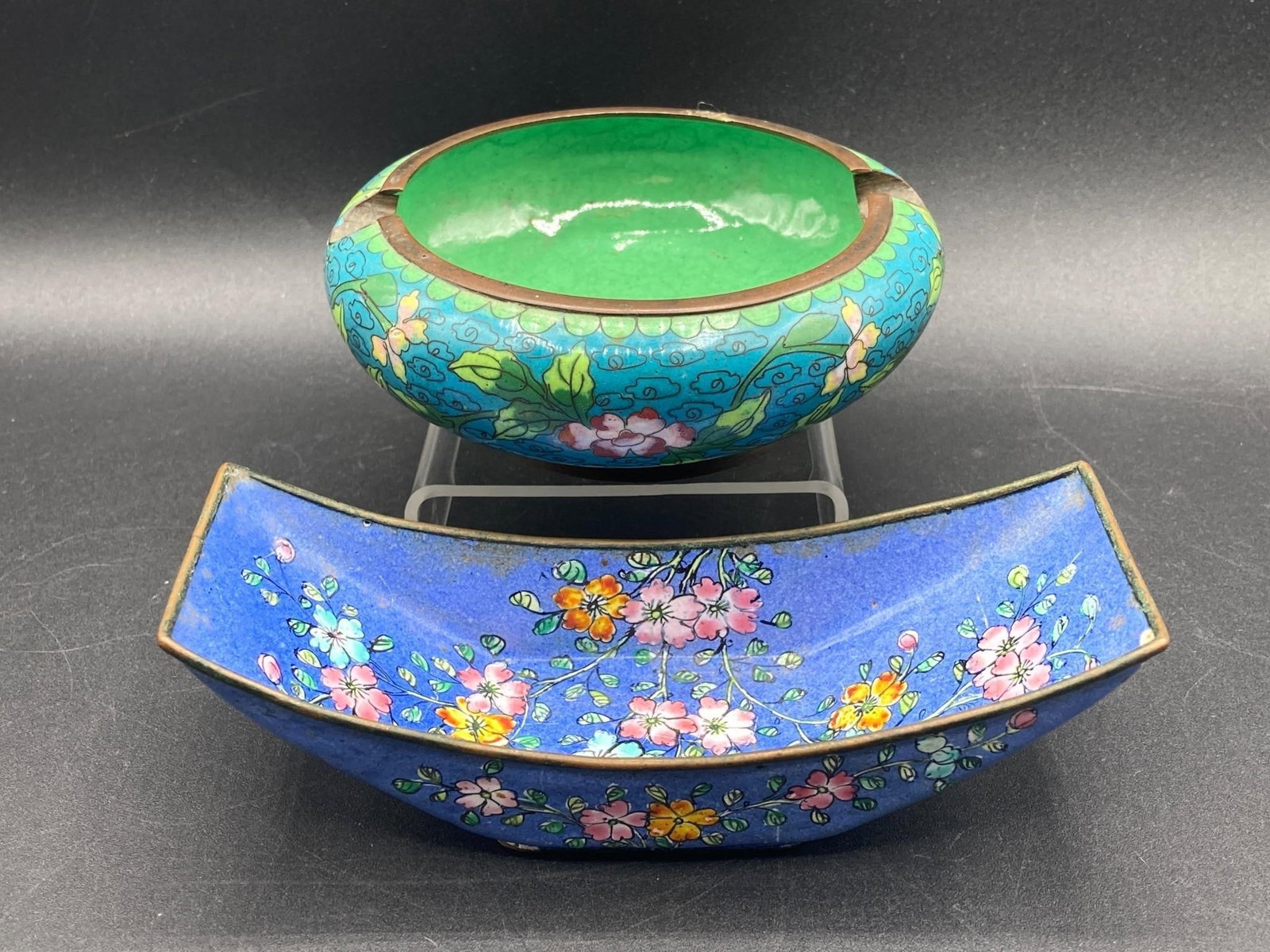 Vintage Chinese Brass Cloisonné Ashtrays: Vintage brass Chinese cloisonné ashtrays. Features flower designs on brass metal. Ashtrays measure from 4.5" to 5.5" long. Both are in good condition.Measurements: 6" W, 8" L, 2" H Inches, 1 pound