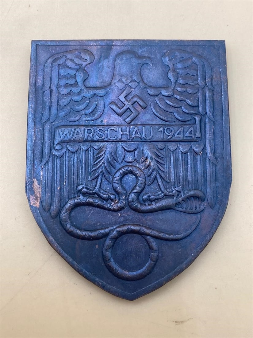 German WWII 1944 Warsaw Battle Arm Shield: German world war II Warsaw 1944 battle uniform arm shield. Issued to soldiers who fought in the battle, worn on arms of uniform tunics. Three prong back. Measures 2" wide and 2 1/2" long. Some light w