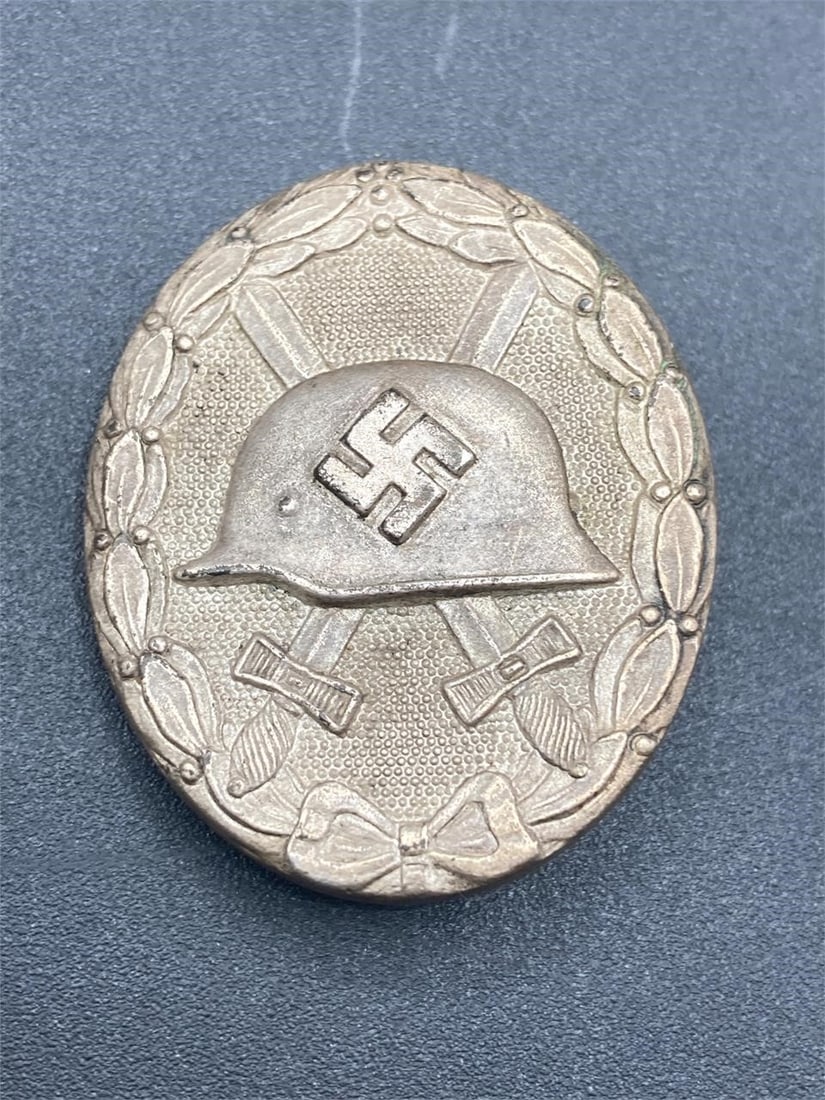 WWII German Wound Badge In Silver: World war II German silver wound badge. Features NSDAP helmet and swords design front. Number 65 on back noted in photos. Measures 1 3/4" long. Some light tarnish on front, visible tarnish on back. Ov