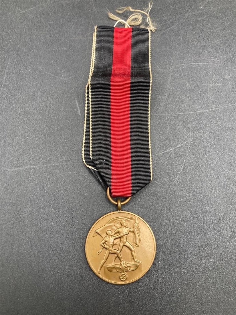 WWII German Sudetenland Annexation Medal: World War II German Sudetenland annexation medal with red ribbon. Issued to participants in the annexation of Czechoslovakia on October 1, 1938. Medal measures 1 1/4". Some light fraying at top of rib