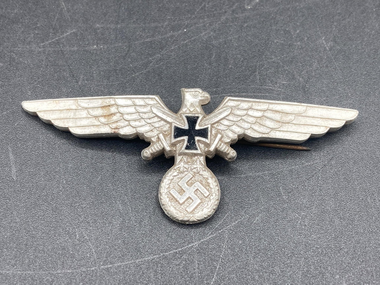WWII German Veteran's Visor Cap Eagle: World War II German veteran's visor cap eagle badge. Eagle, two swords, iron cross and NSDAP symbol design. 2 GES GESCH stamp on back noted in photos. Measures 3 3/4" wide. Badge is in excellent condi