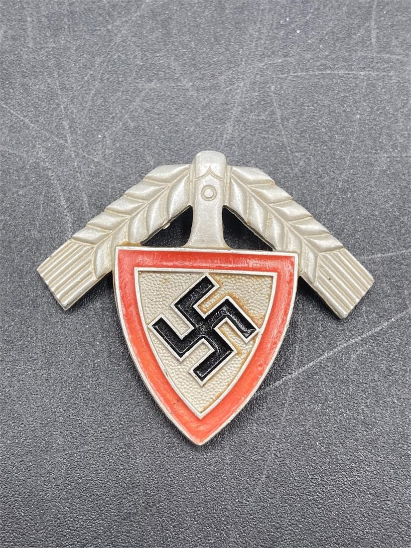 1937 German RAD National Labor Corp Cap Badge: 1937 German labor corps (RAD) member cap badge. Aluminum material with painted NSDAP symbol and shield. GES GESCH, 37 and M.H. maker stamps on back. Measures 1 1/2" long. Pin is in excellent condition