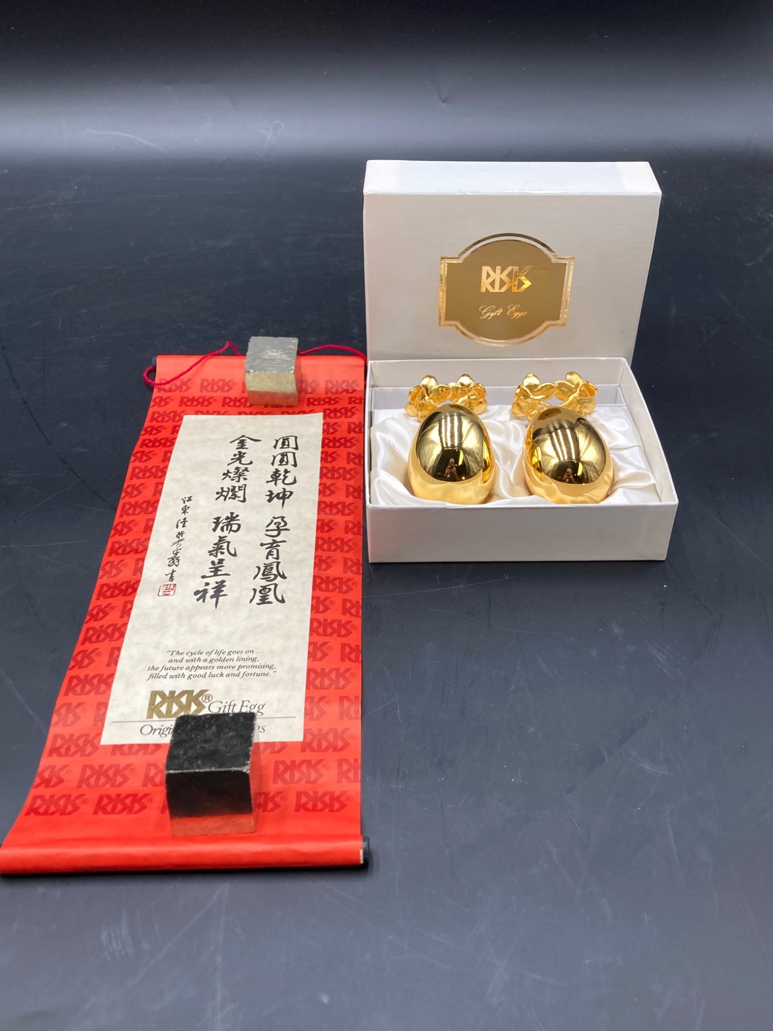 Risis Of Singapore 24kt Gold Plated Gift Egg Set: This Risis gift set includes two 24kt gold plates eggs accompanied by three-point floral gold-tone display stands. The eggs feature a polished reflective finish, and the set is presented in its origin