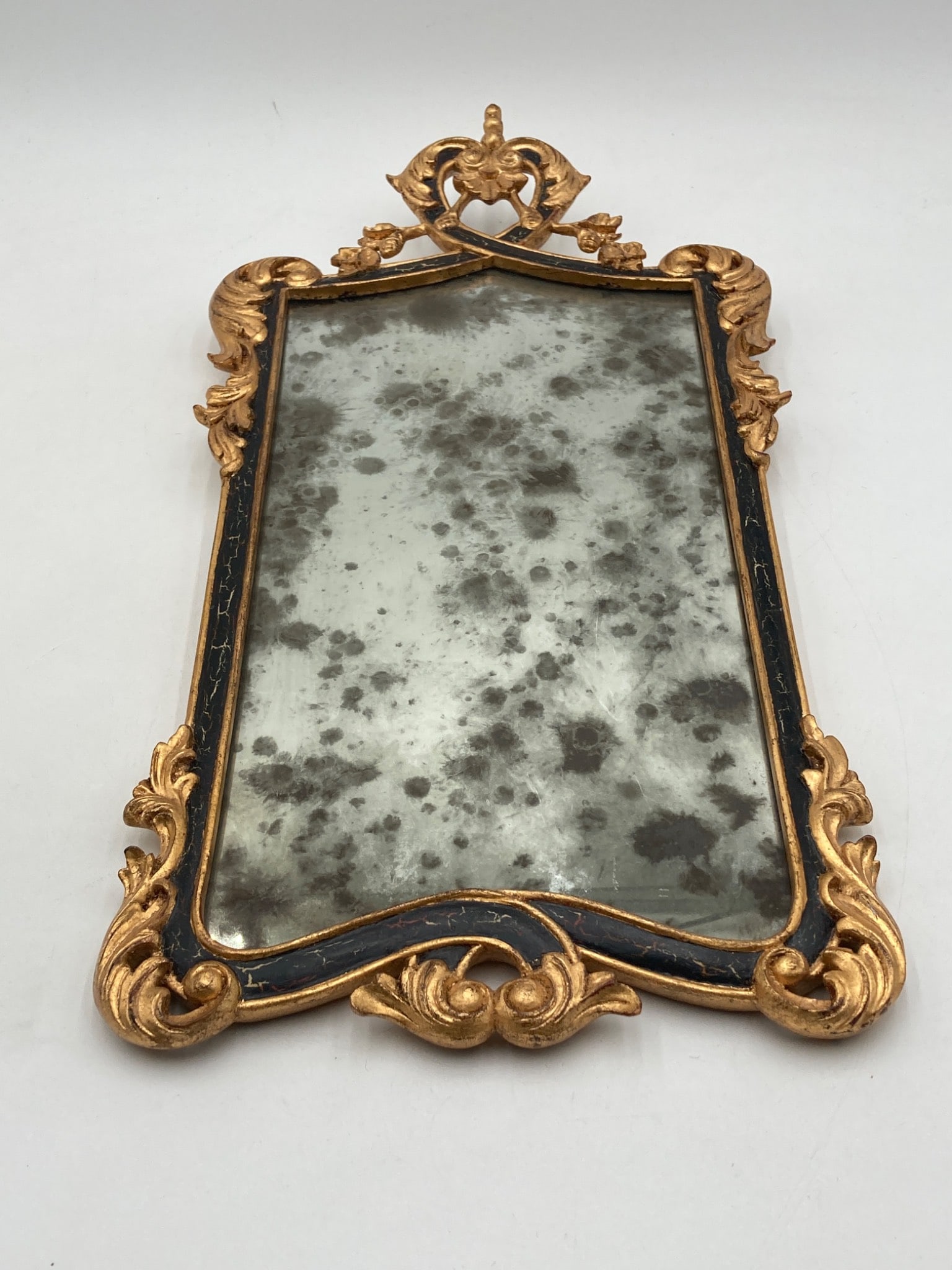 Antique French Giltwood Mirror: This antique French giltwood mirror features an ornately sculpted frame with intricate leafy and scroll motifs. The frame combines a black-painted ebonized finish with gilt detailing. The mirror exhib