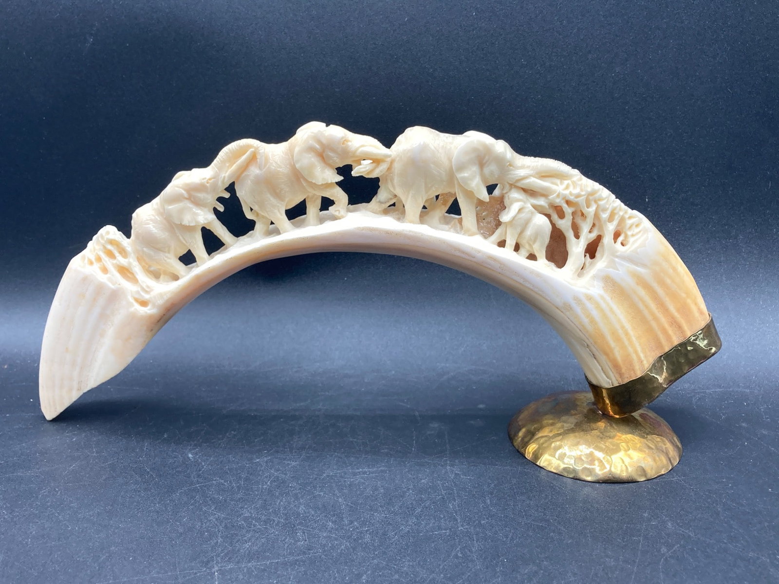 Carved Faux Animal Tusks With Elephant Motif: This is a carved faux ivory tusk sculpture featuring an elephant procession motif. The tusk carving depicts multiple elephants walking in line with intricate tree and nature details. The tusk is mount