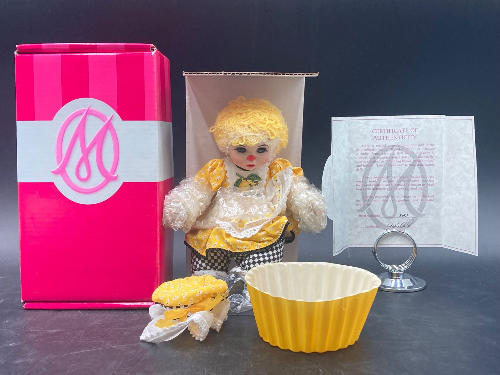 Marie Osmond Rag-a-Muffin Lemon Poppyseed Doll Collectible Set: This listing is for a "Marie Osmond Rag-a-Muffin Lemon Poppyseed Doll" collectible complete with its original components. The set includes: | | 1. **Doll**: This 'Rag-a-Muffin Lemon Poppyseed' doll fe