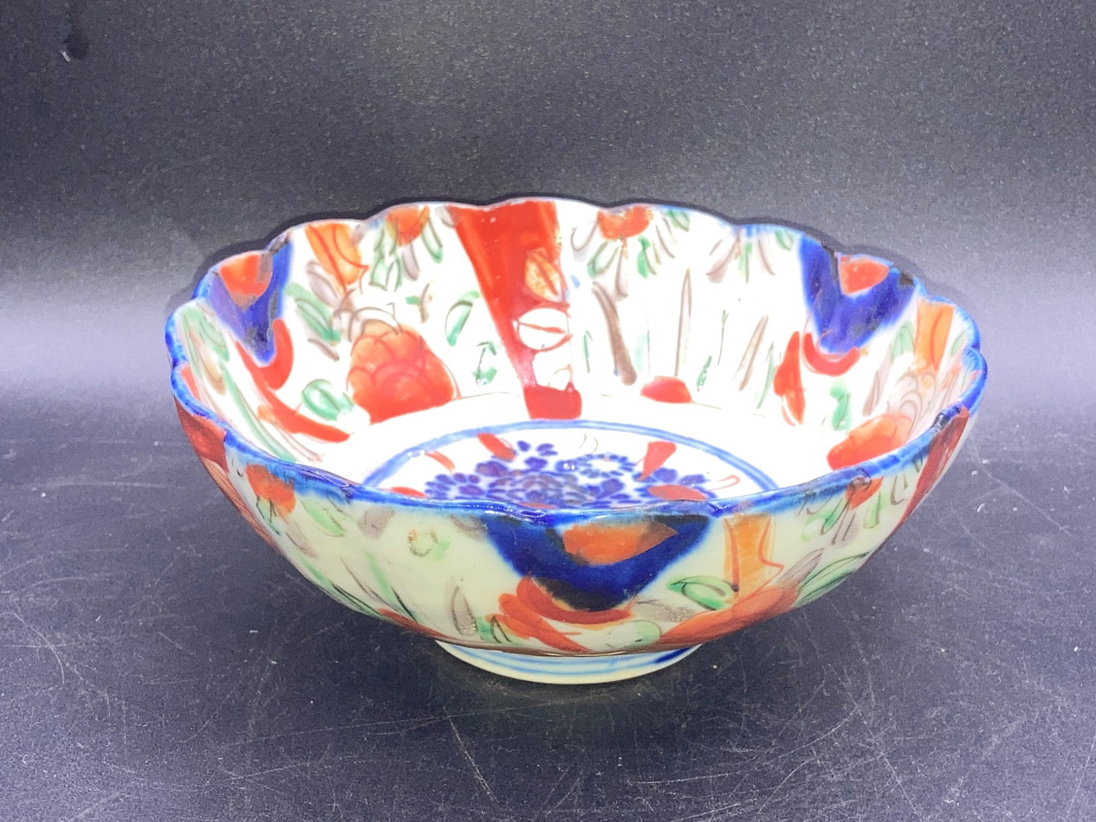 Antique Japanese Imari Porcelain Bowl: This is an antique Japanese Imari porcelain bowl, featuring a hand-painted floral motif in vivid hues of red, blue, green, and orange. The bowl showcases the characteristic Imari scalloped rim, with d