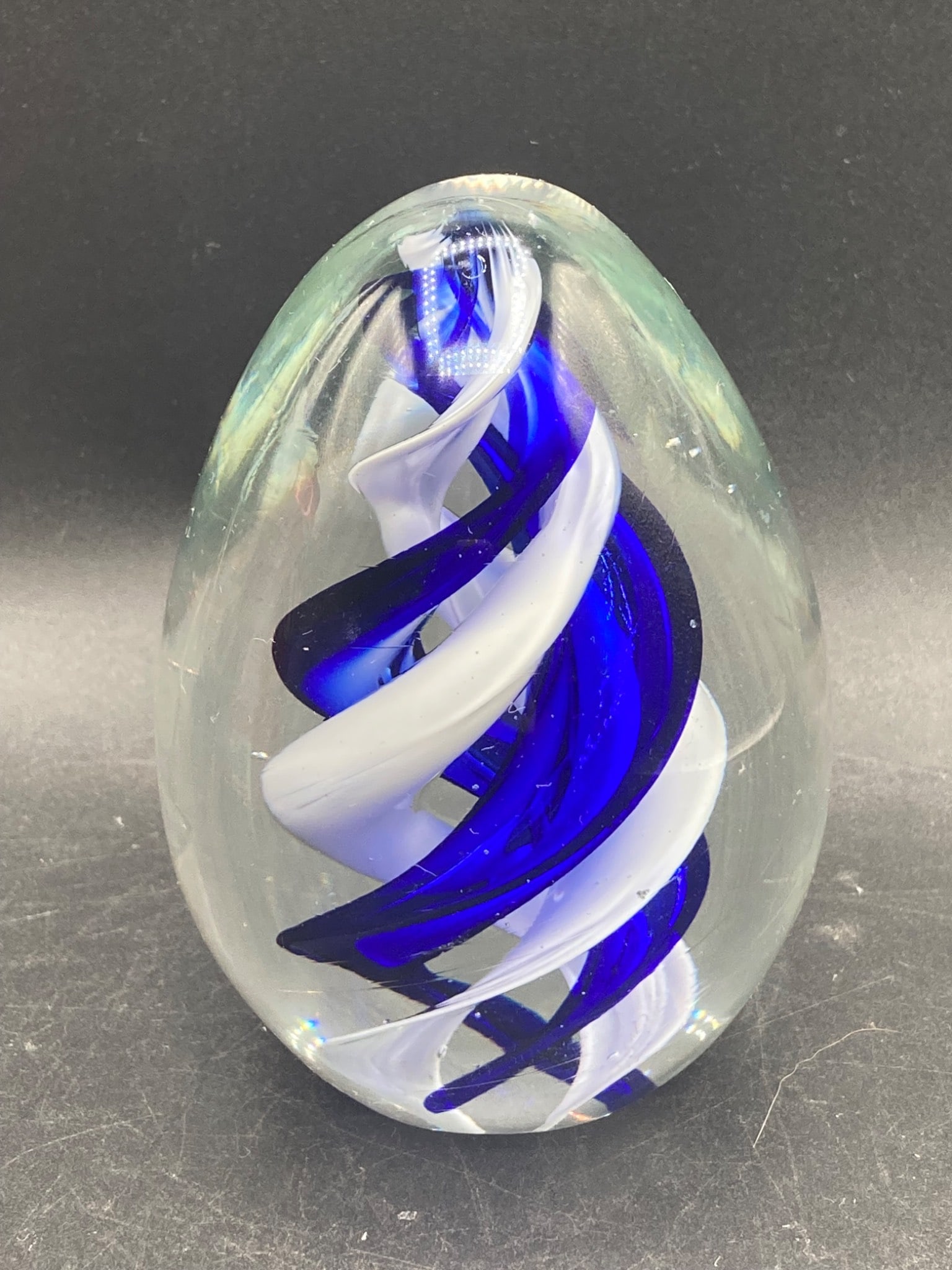 Murano Glass Blue Swirl Paperweight: This is a Murano glass paperweight featuring a blue and white swirl design encased in clear glass. The object originates from Italy, as indicated by the gold sticker marked 'Italy Design' affixed to t