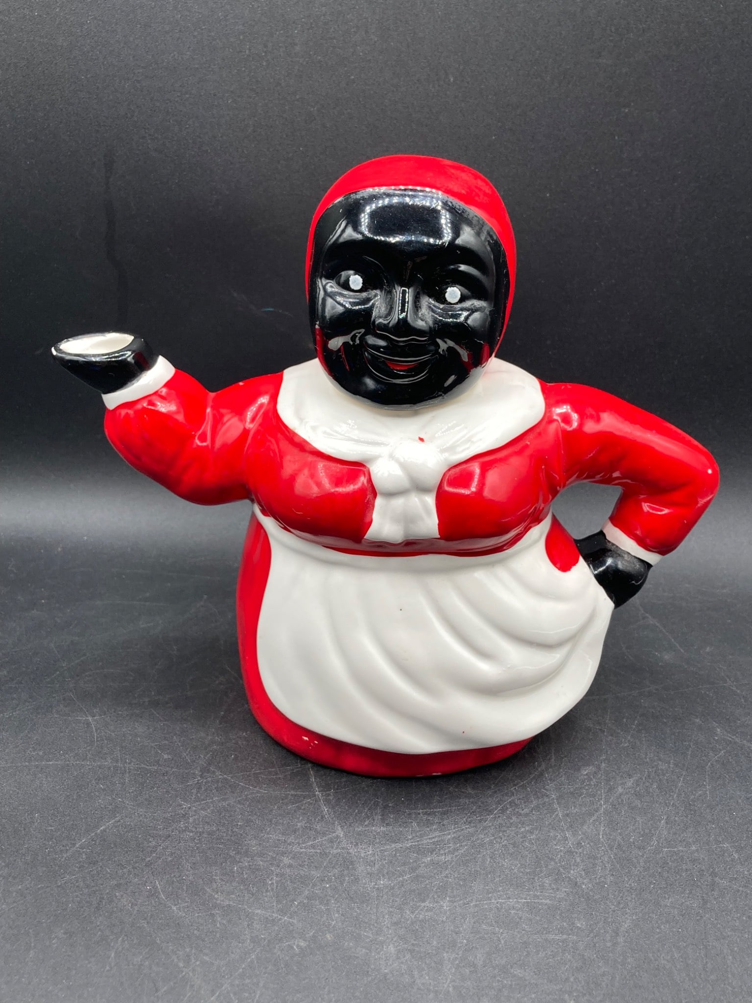 Black Americana Porcelain Teapot: A Black Americana porcelain teapot featuring a figure in red and white attire with a removable head as the lid. The teapot is hand-painted with a glossy finish and measures approximately 7 inches tall