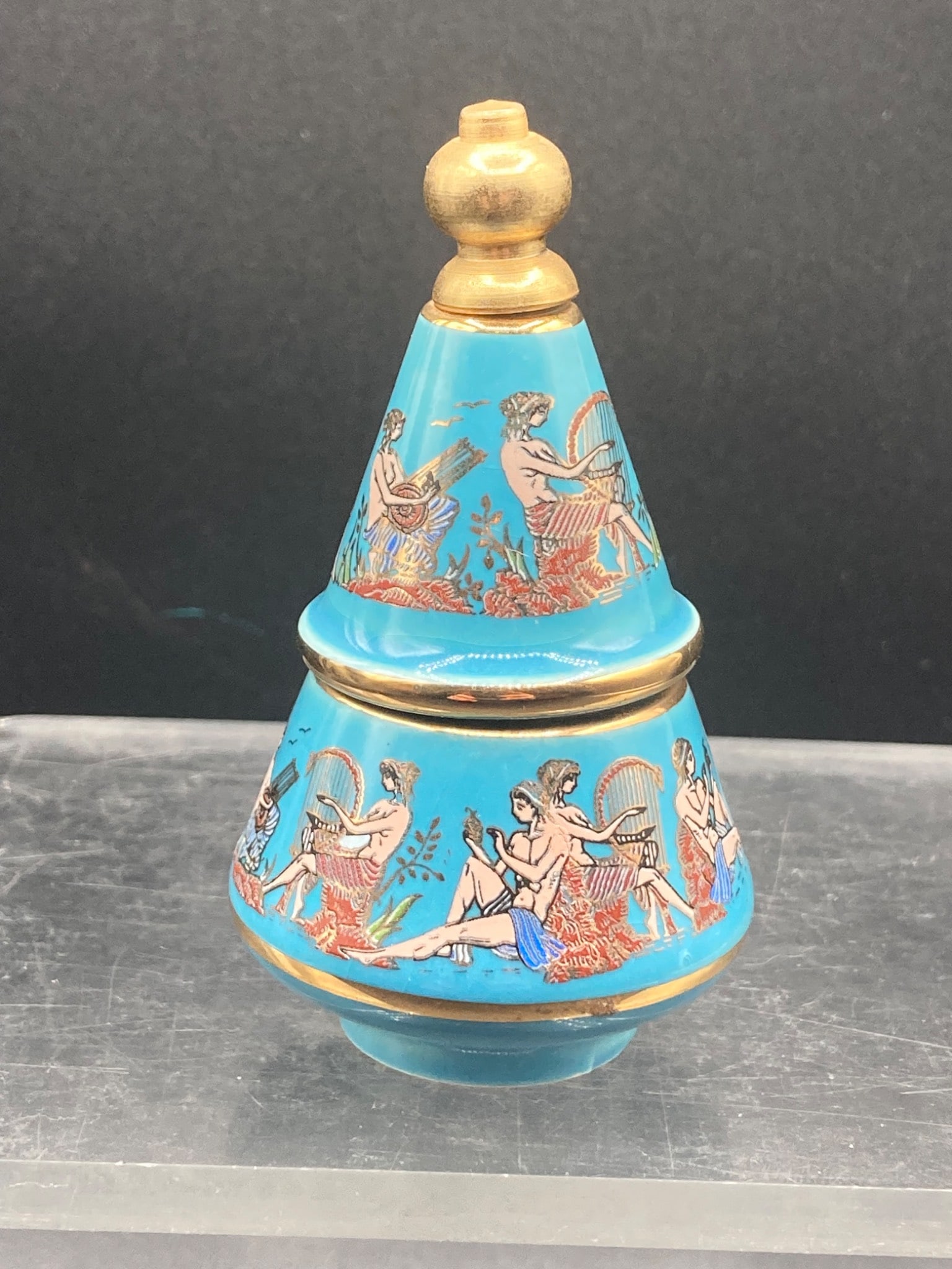 Bardaco Greek Solid Parfum: A ceramic Bardaco Greek solid parfum container featuring classical design elements. The container is vividly decorated with depictions of classical Greek figures playing harps and other instruments. T