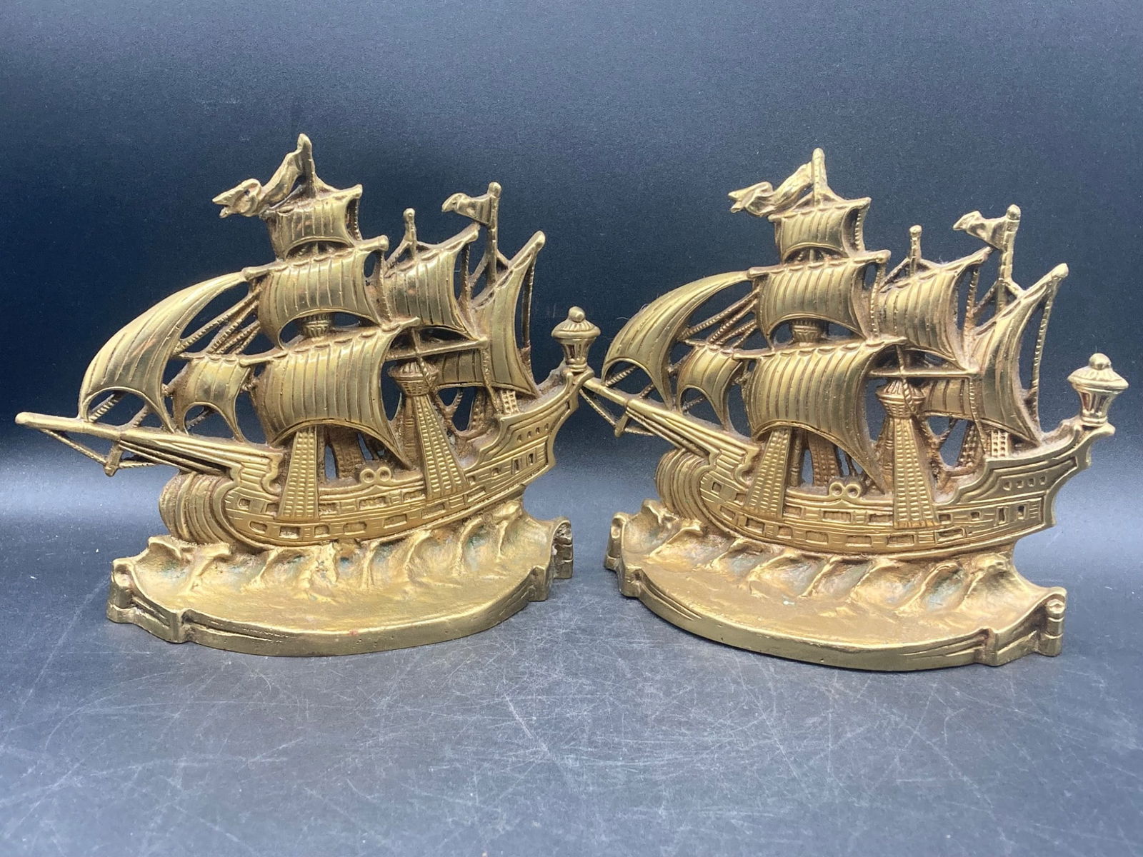 Antique Boston Nickel Plating Company Ship Bookends: A pair of cast metal ship-designed bookends manufactured by Boston Nickel Plating Company. The bookends depict detailed sailing ships atop ocean waves and are stamped on the reverse with ˜Mfd by