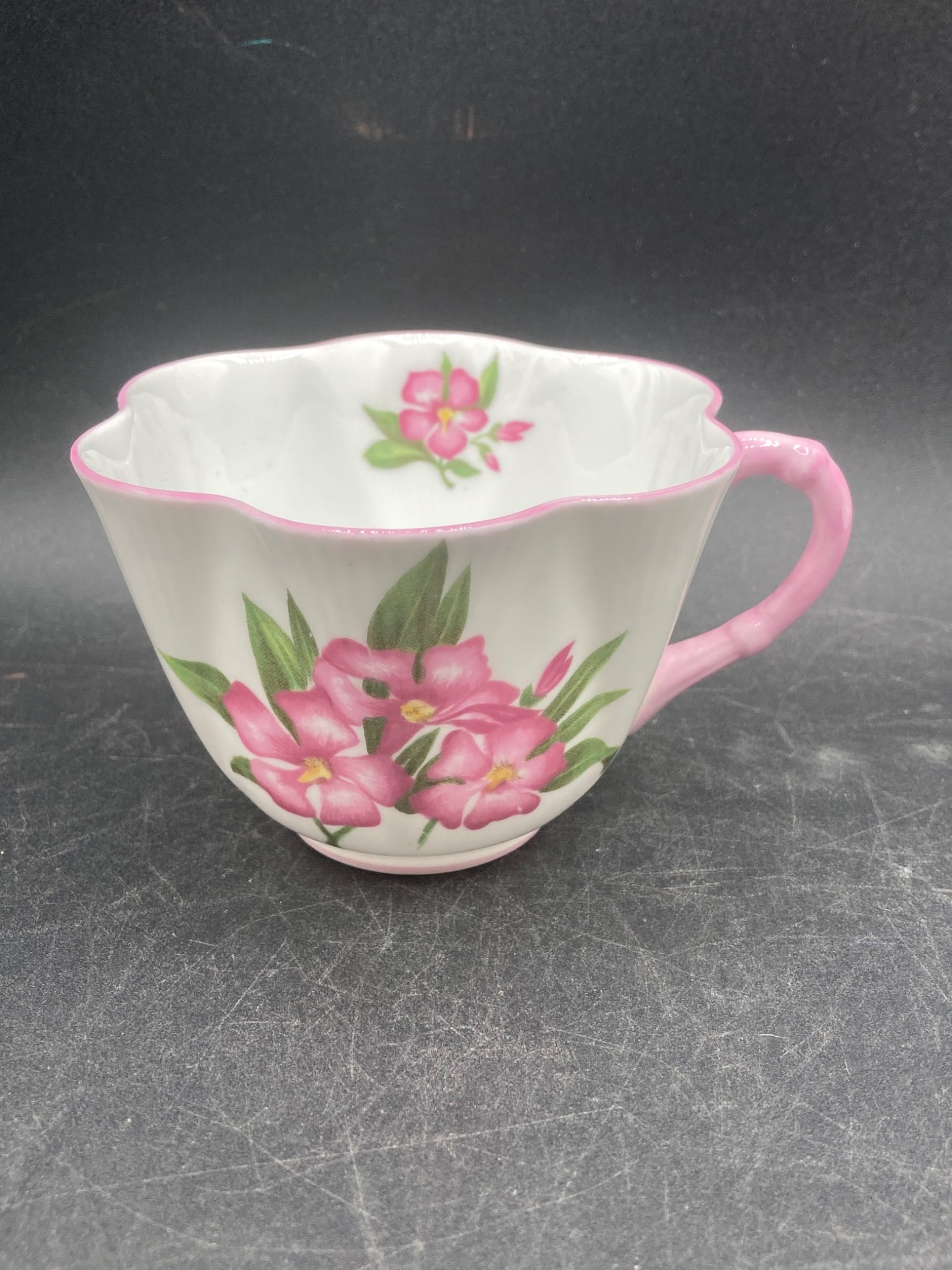 Shelley England Bone China Oleander Tea Cup & Saucer: This tea cup and saucer set is made by Shelley England in fine bone china. The pattern is ˜Oleander™ with the pattern number 13883, featuring pink floral decorations on a scalloped cup and matching