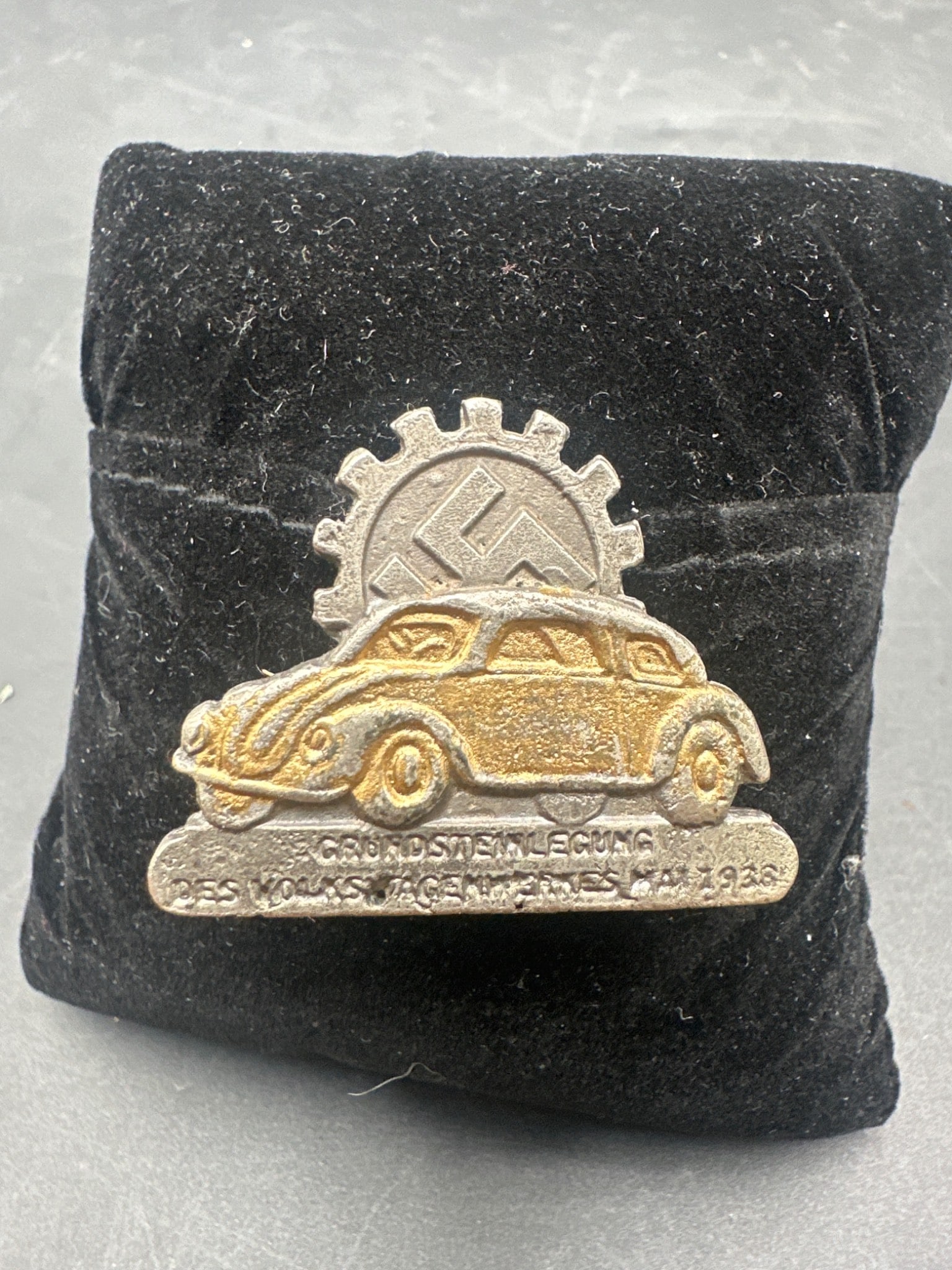 1938 WWII German Fallersleben Volkswagen Factory Cornerstone Laying Ceremony Badge: This is a 1938 badge issued for the cornerstone laying ceremony of the Volkswagen factory in Fallersleben, Germany. The front displays a vehicle relief with text 'Grundsteinlegung Des Volkswagen-Werke