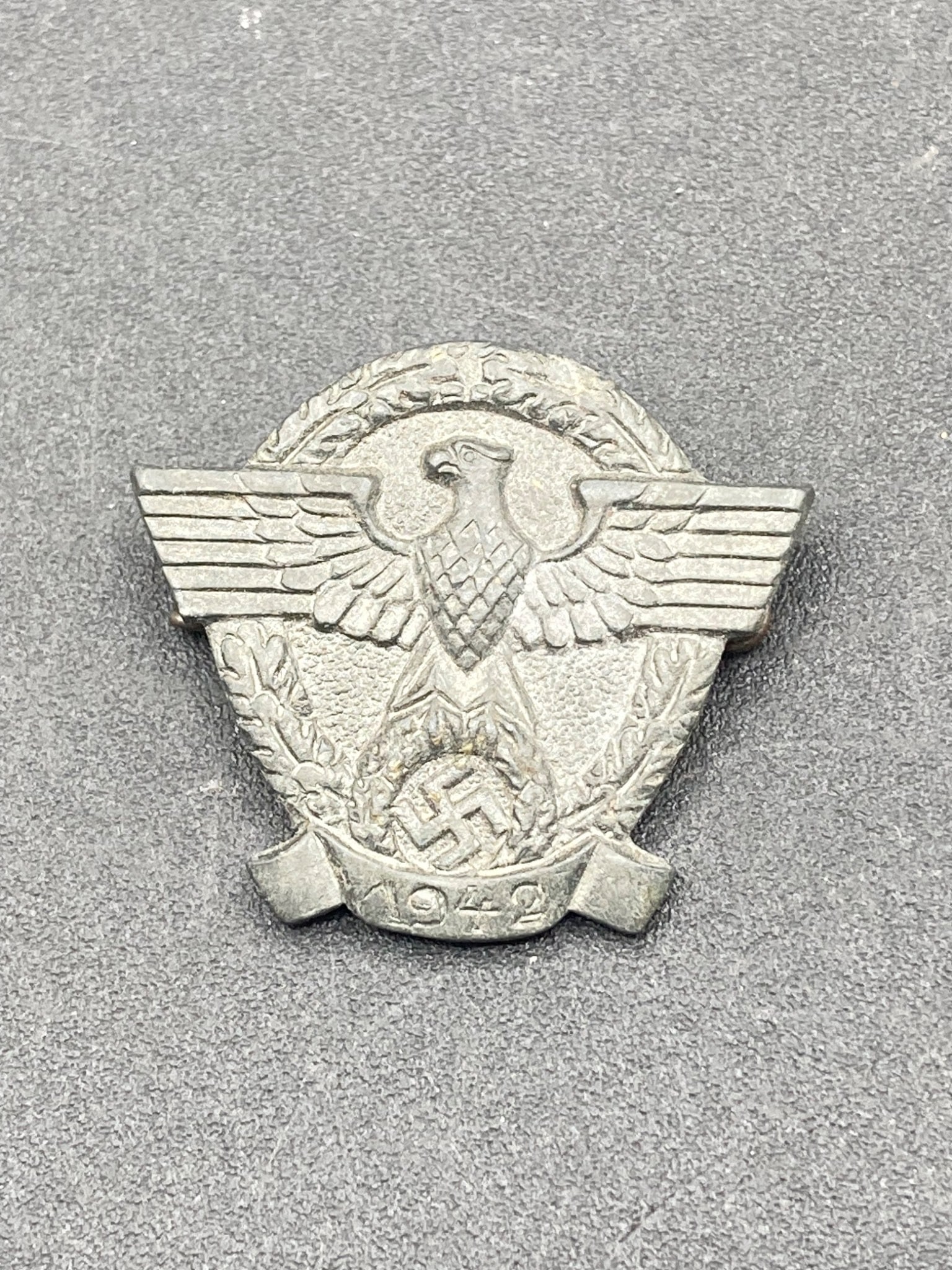 1942 German NSDAP Police Tinnie Badge: This is a 1942-dated German NSDAP Police tinnie featuring a central eagle motif holding a wreath containing a swastika. The reverse side includes a 'P6' marking and a functional pin clasp. The dimensi