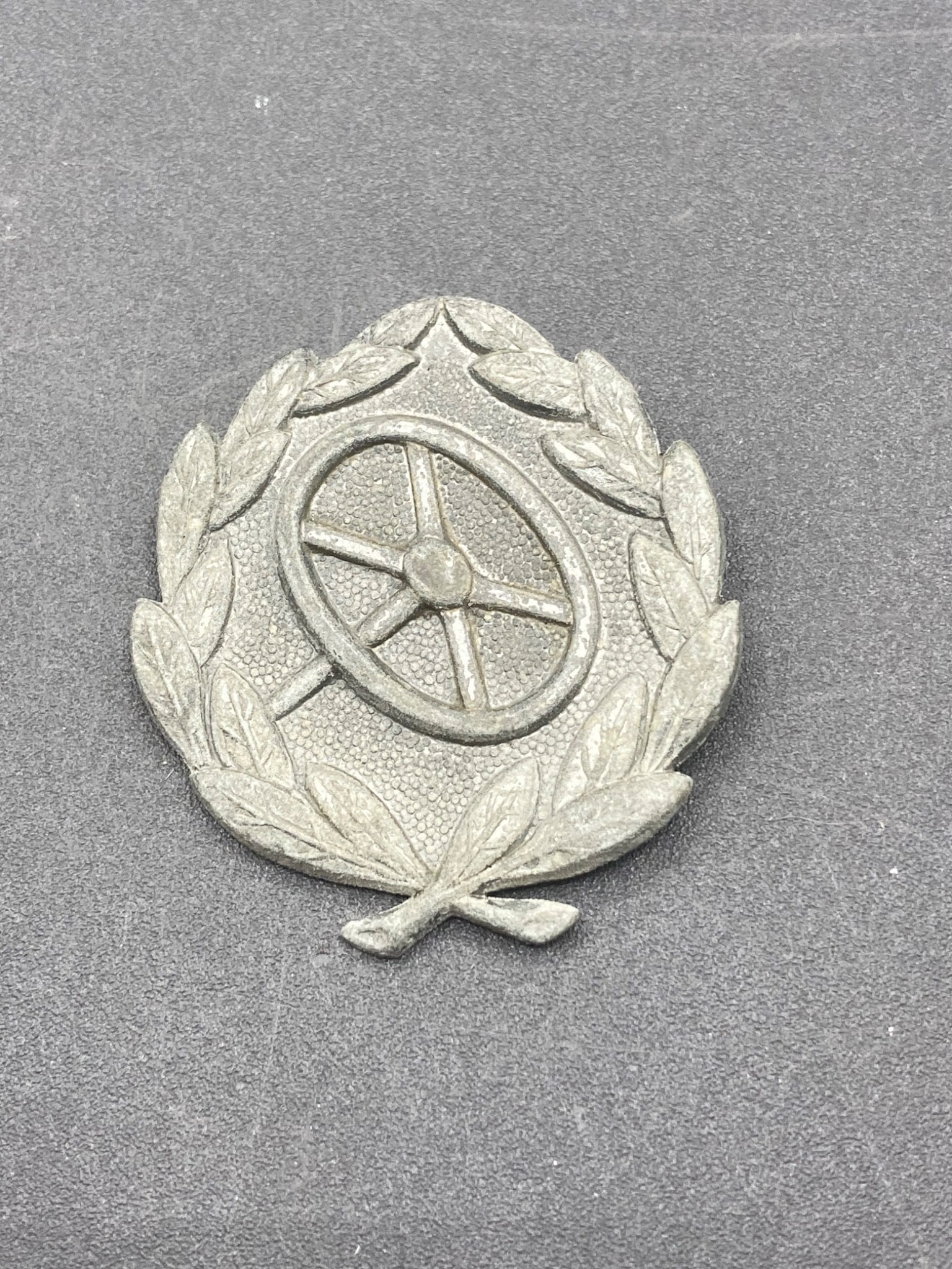 WWII German Wehrmacht Driving Proficiency Badge in Silver: This is a WWII-era German Wehrmacht Driving Proficiency Badge in Silver. The badge consists of a laurel wreath enclosing a steering wheel, symbolizing proficiency in vehicle operation. Measuring 1.75"