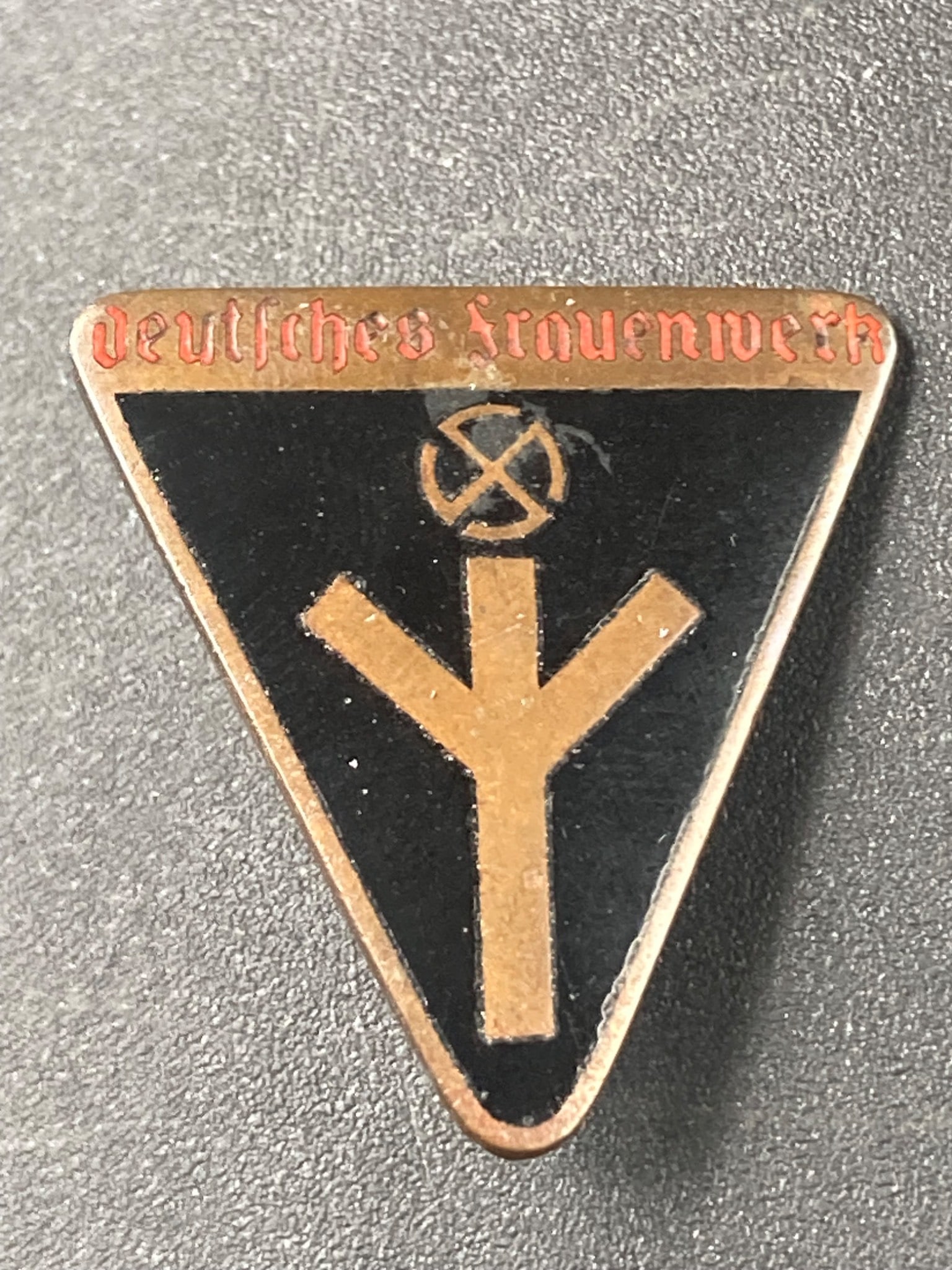 WWII German Frauenwerk Badge: This is a WWII German Frauenwerk Badge featuring a triangular design with black enamel and the 'deutsches Frauenwerk' text. The reverse side showcases a functional pin-back mechanism and markings, inc