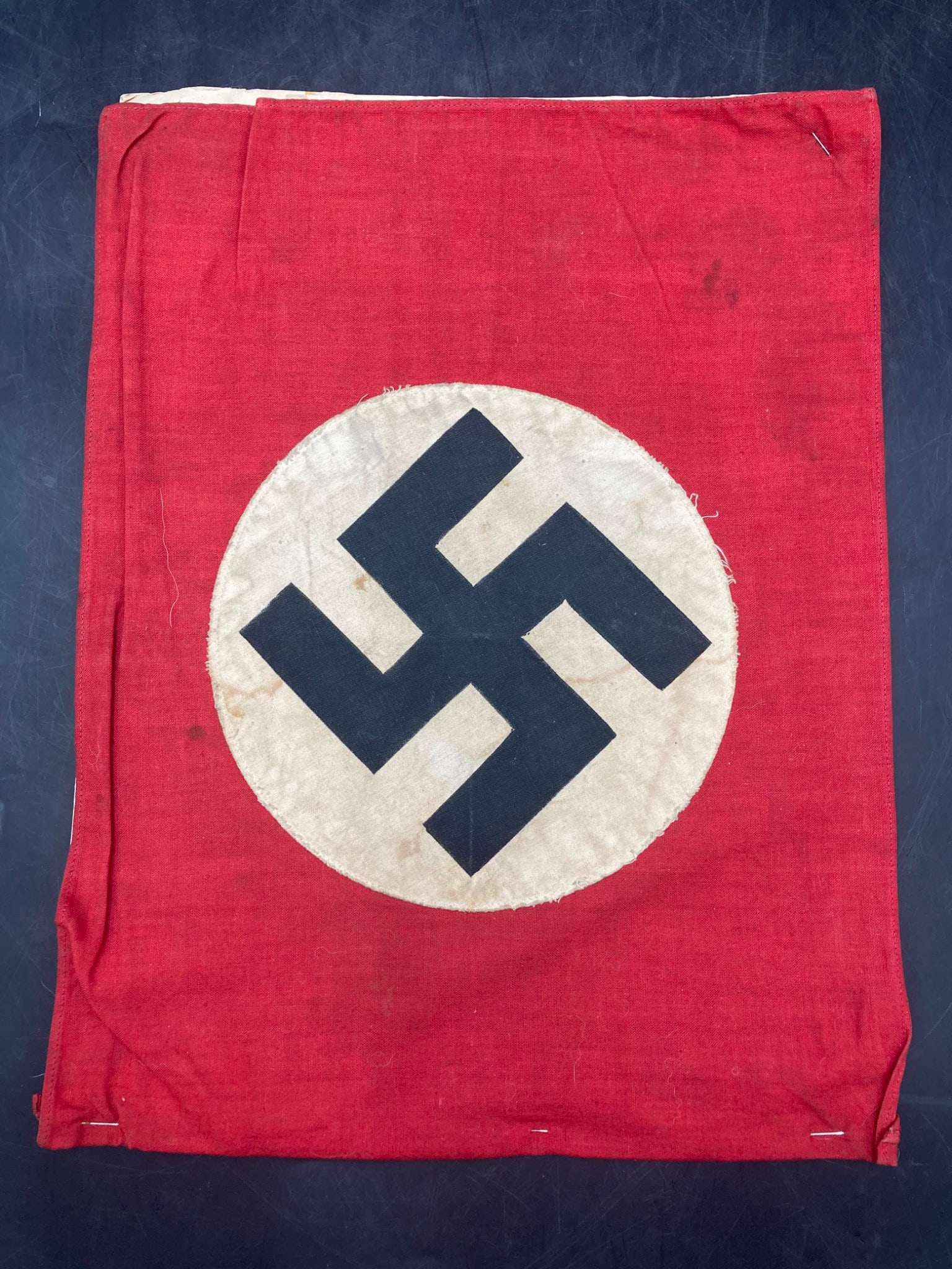 Original 11×14 Inch WWII German NSDAP Flag: An original WWII-era German NSDAP flag measuring approximately 11x14 inches. The flag features a red background with a central white circle containing a black NSDAP emblem. Cotton material with single