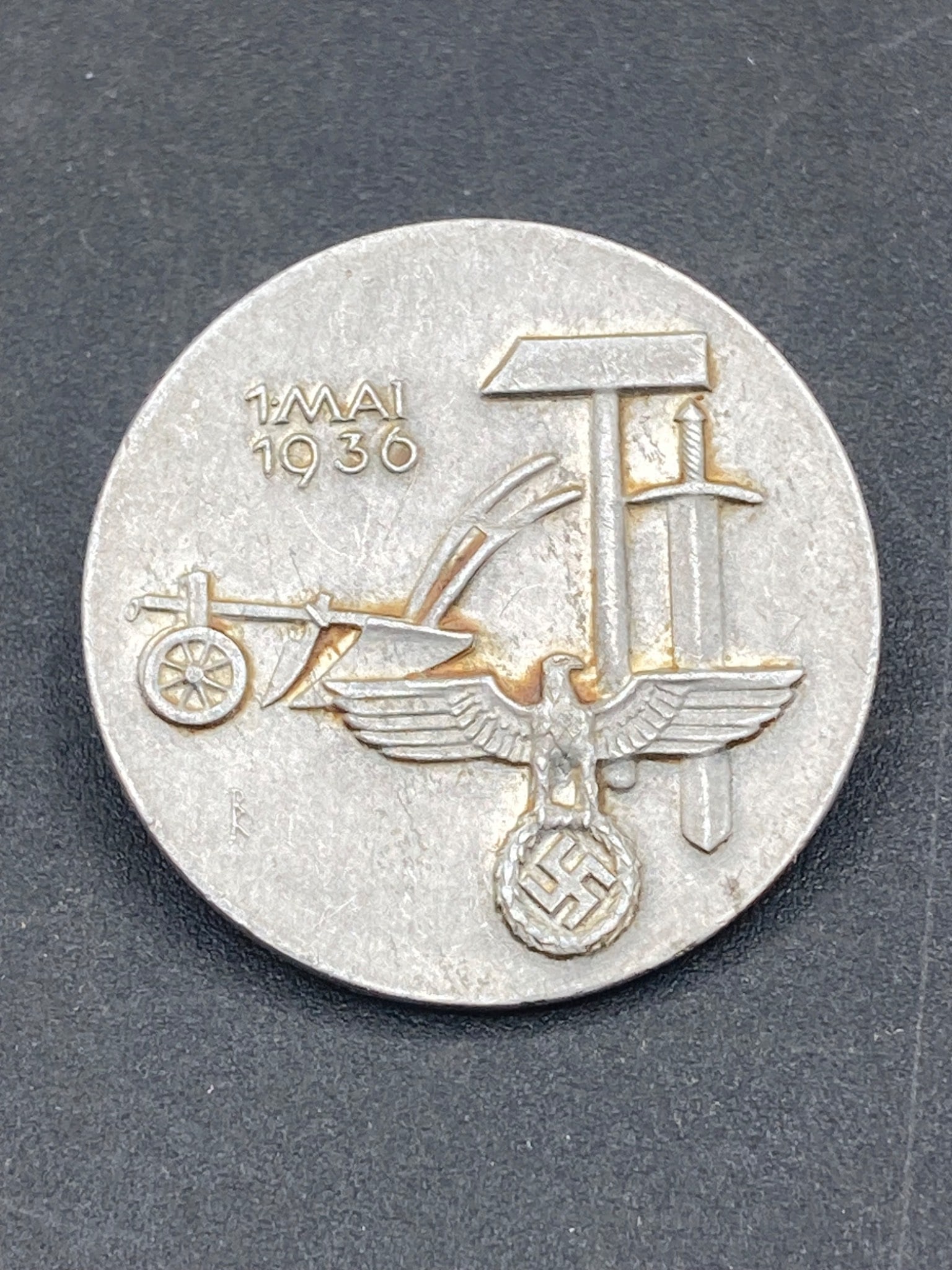 1936 German May Day Tinnie, K. Frank Nürnberg: This is a circular 1936 German May Day tinnie marked with 'K. Frank Nürnberg' on the reverse side. The front of the pin displays a hammer, sickle, and sword design above an eagle perched atop a swast