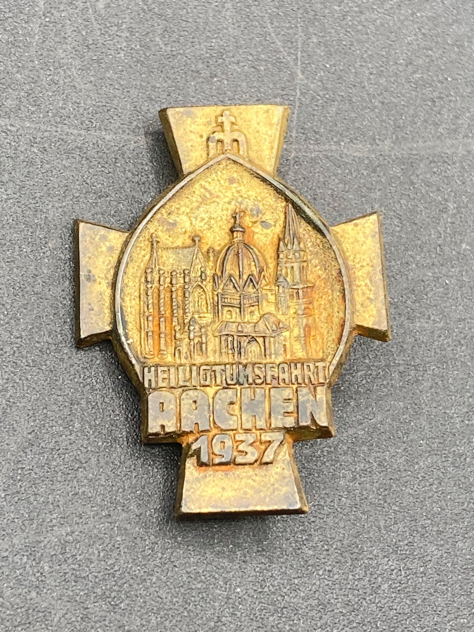 1937 Aachen Cathedral Pilgrimage Tinnie in Cross Design: A single 1937 Aachen Cathedral Pilgrimage Tinnie made from pressed metal in a cross-style design. Features a detailed raised image of the Aachen Cathedral on the front, with 'HEILIGTUMSFAHRT AACHEN 19