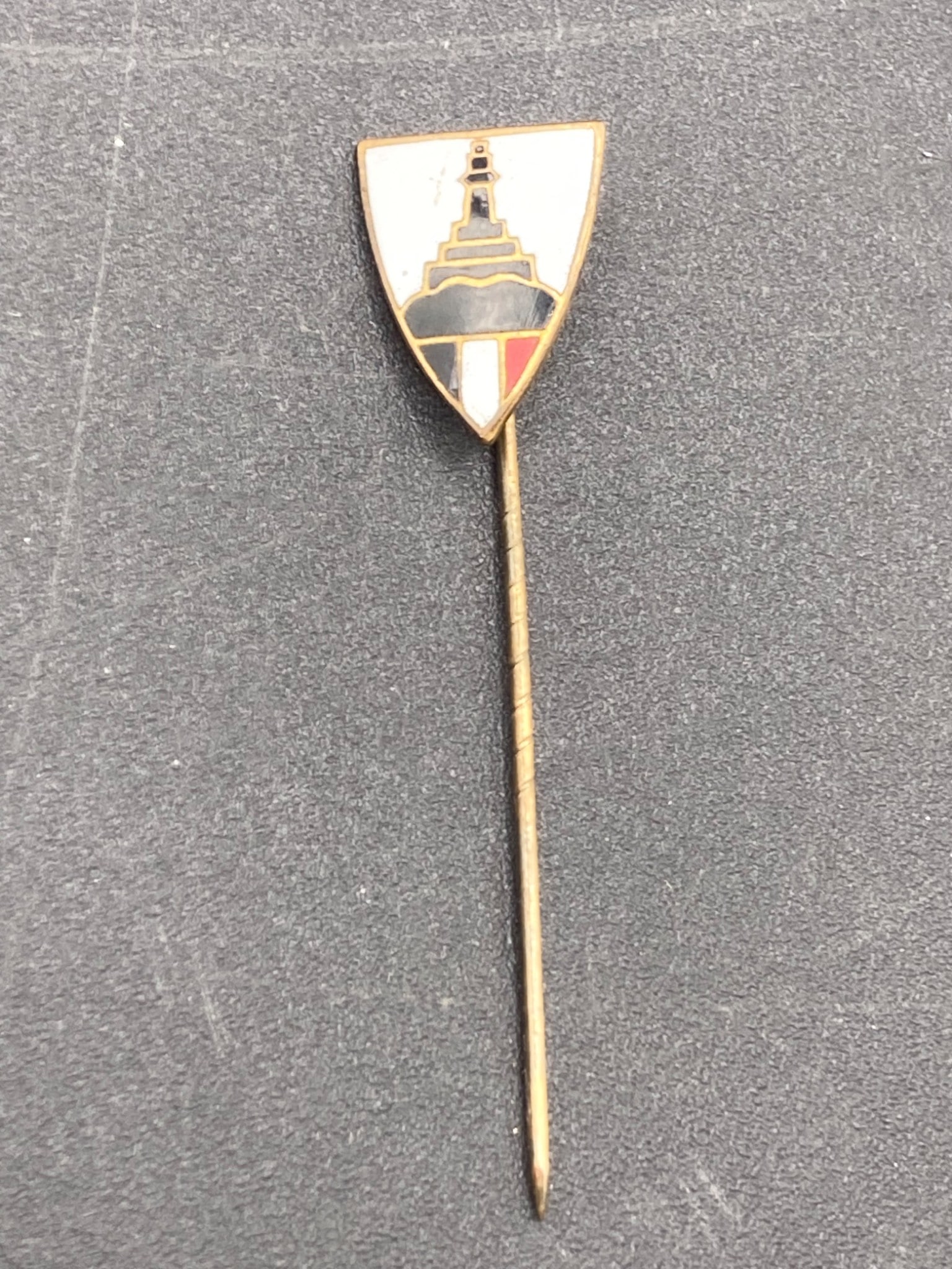 WWI Imperial German DKRB Veteran Stickpin with Enamel Shield Design: A WWI Imperial German DKRB veteran stickpin featuring a gold-tone body and a shield-shaped enamel insignia depicting a monument and German national colors. The reverse is stamped "Ges. Gesch," indicat