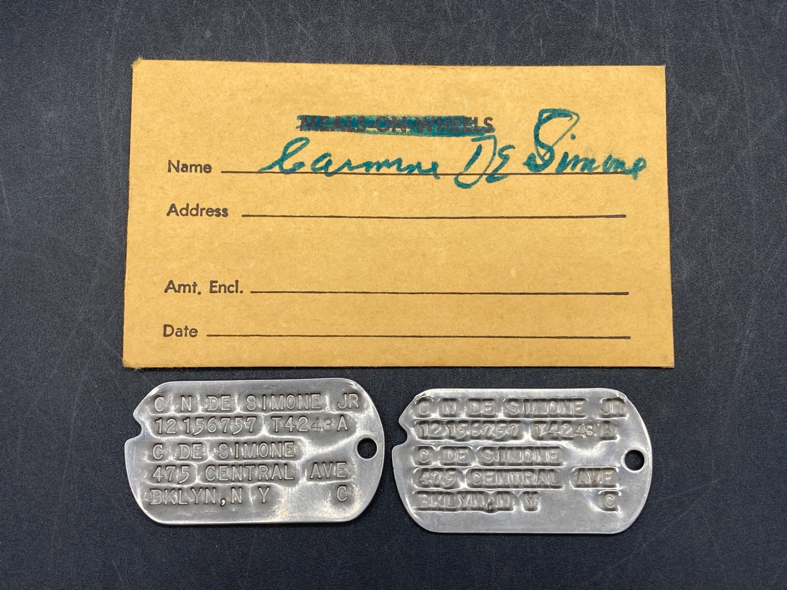 WWII United States Army Dog Tags with Pouch: A pair of WWII-era United States Army dog tags belonging to an individual named 'C.N. De Simone Jr' with serial number 12156757 and service designation 'T4243-A.' The dog tags include the address '475